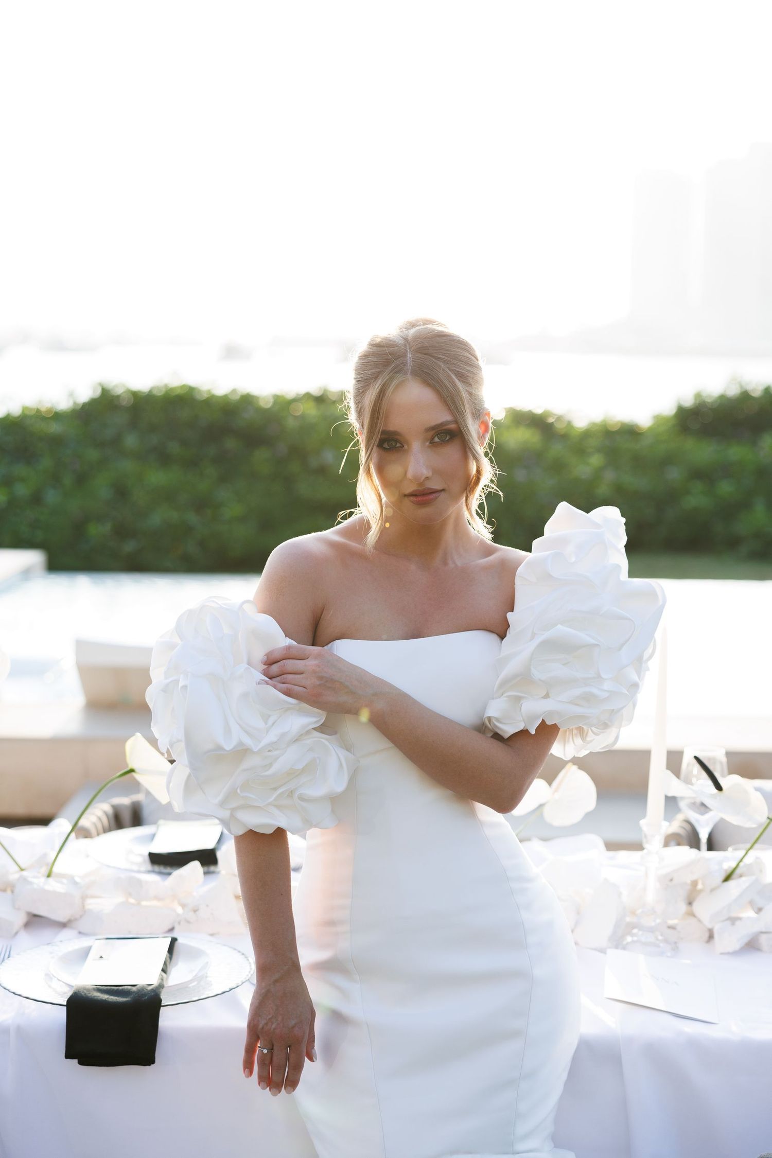 Bride in an off-shoulder white gown with ruffled details poses at an outdoor reception.