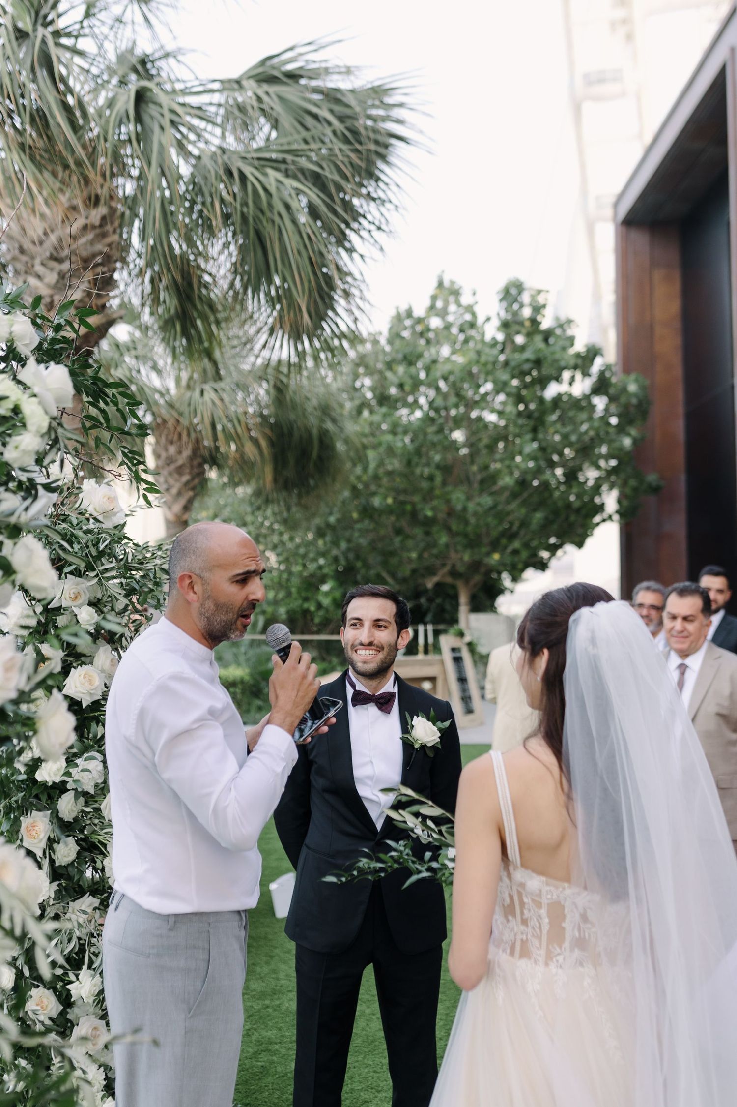 Wedding party members react emotionally during outdoor ceremony with white floral decorations.