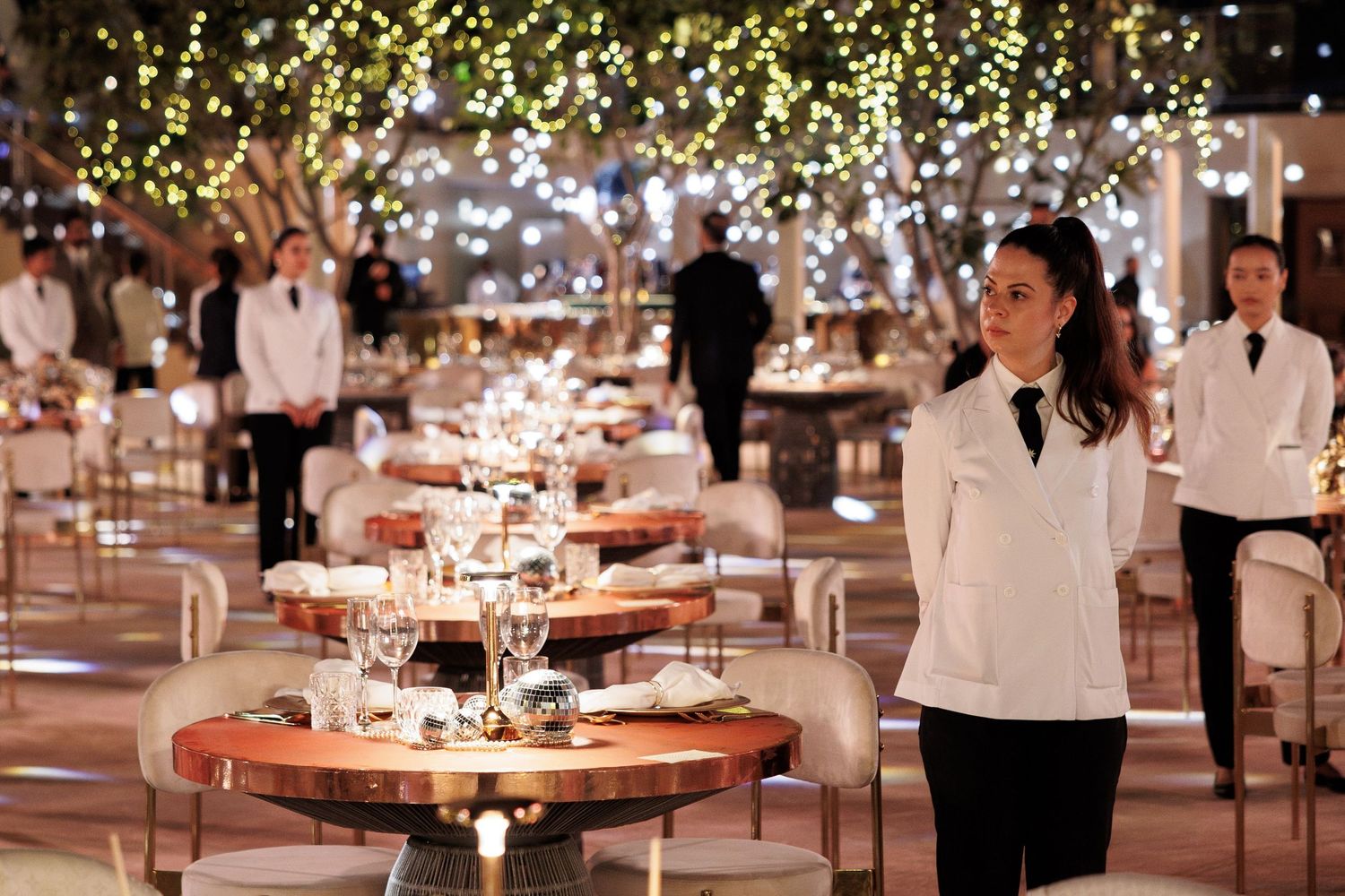 Upscale restaurant interior with elegant table settings and staff in white uniforms.