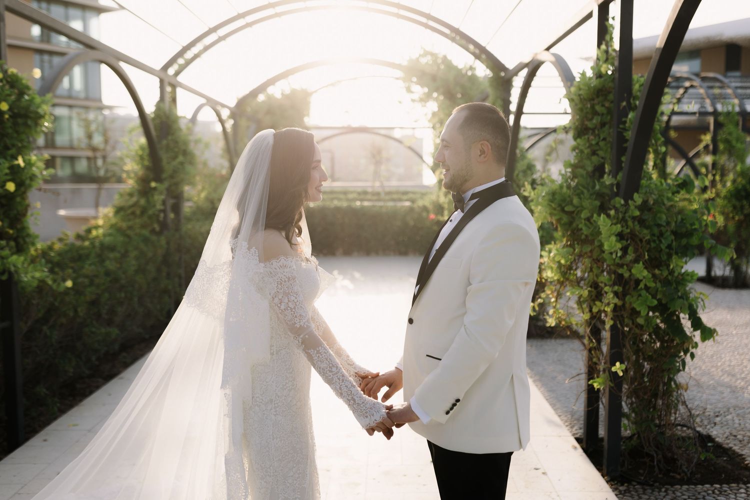 Couple holding hands in a romantic garden setting with soft sunlight filtering through.