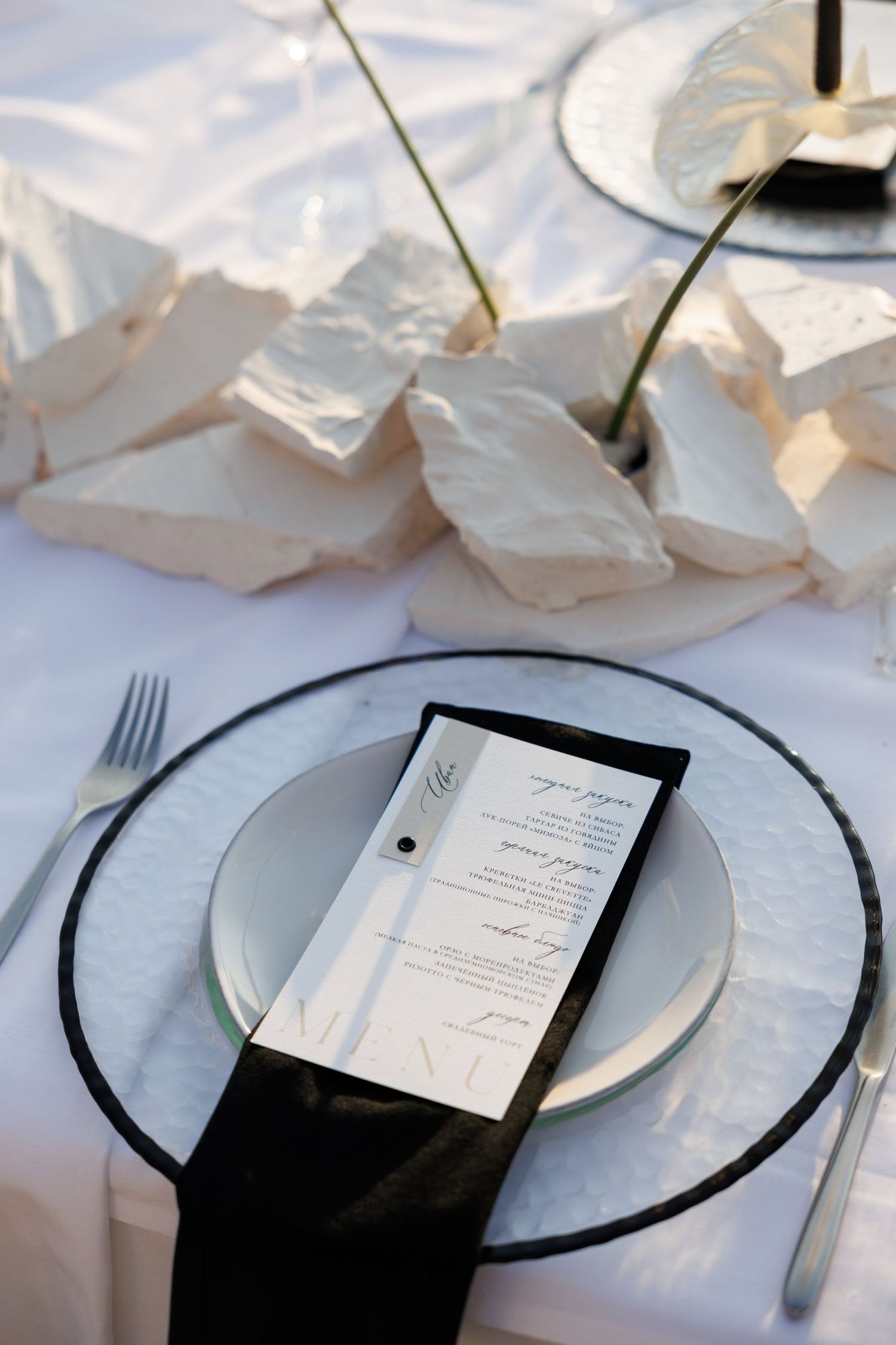 Wedding place settings with white plates, menus, and silverware on crisp linens.