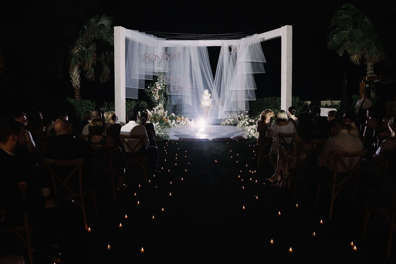 Outdoor wedding reception setup with string lights and white draping creating a romantic ambiance.