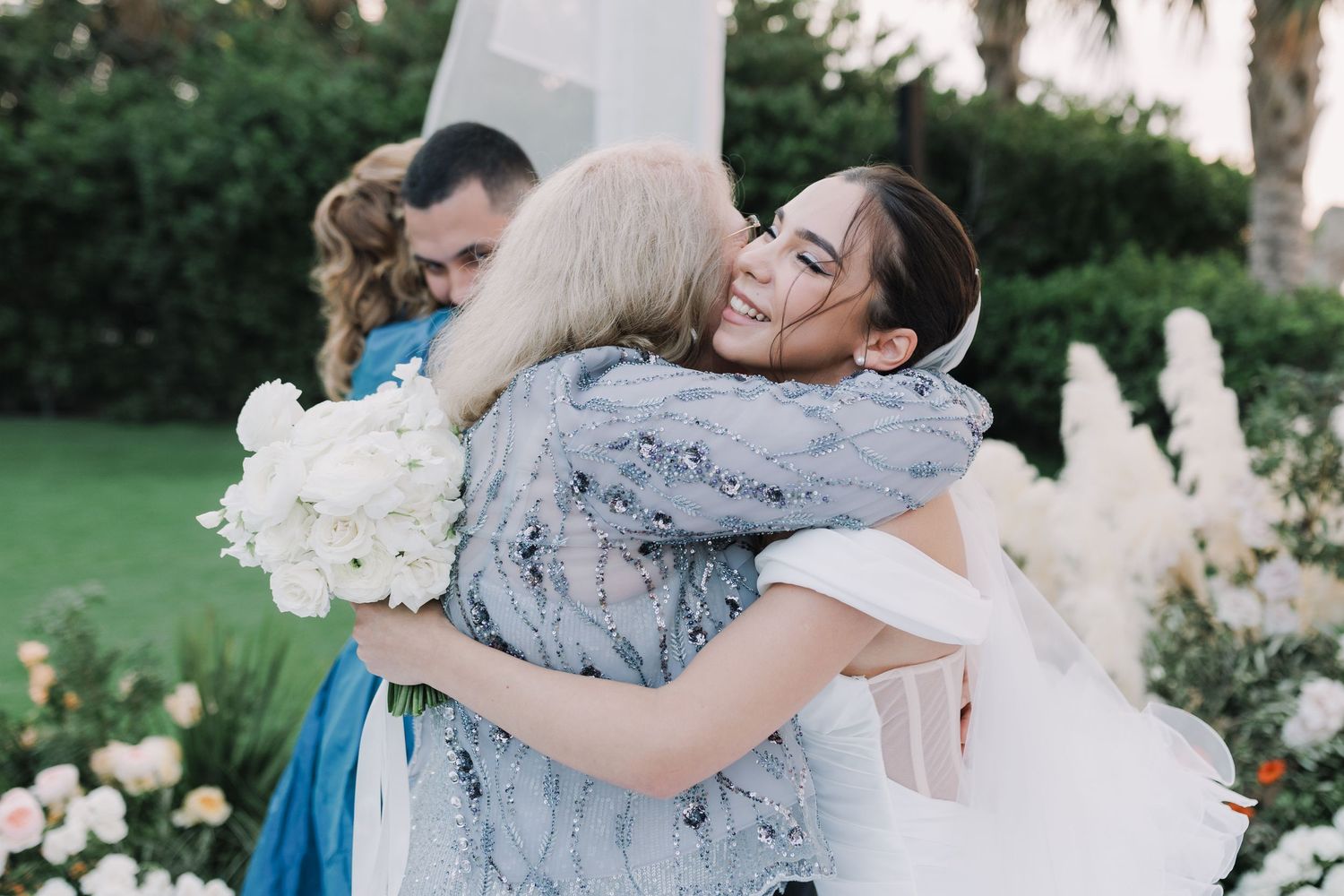 Celebratory hugs and embraces at an outdoor wedding with floral decorations.