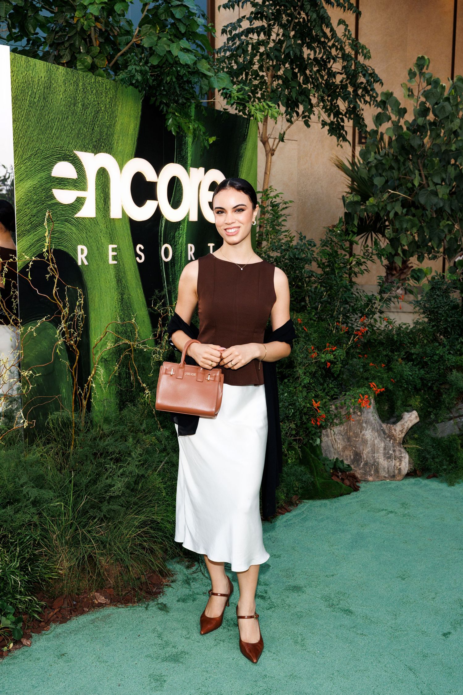 Stylish outfit featuring a brown sleeveless top, white midi skirt, brown leather bag and heels at Encore Resort event.