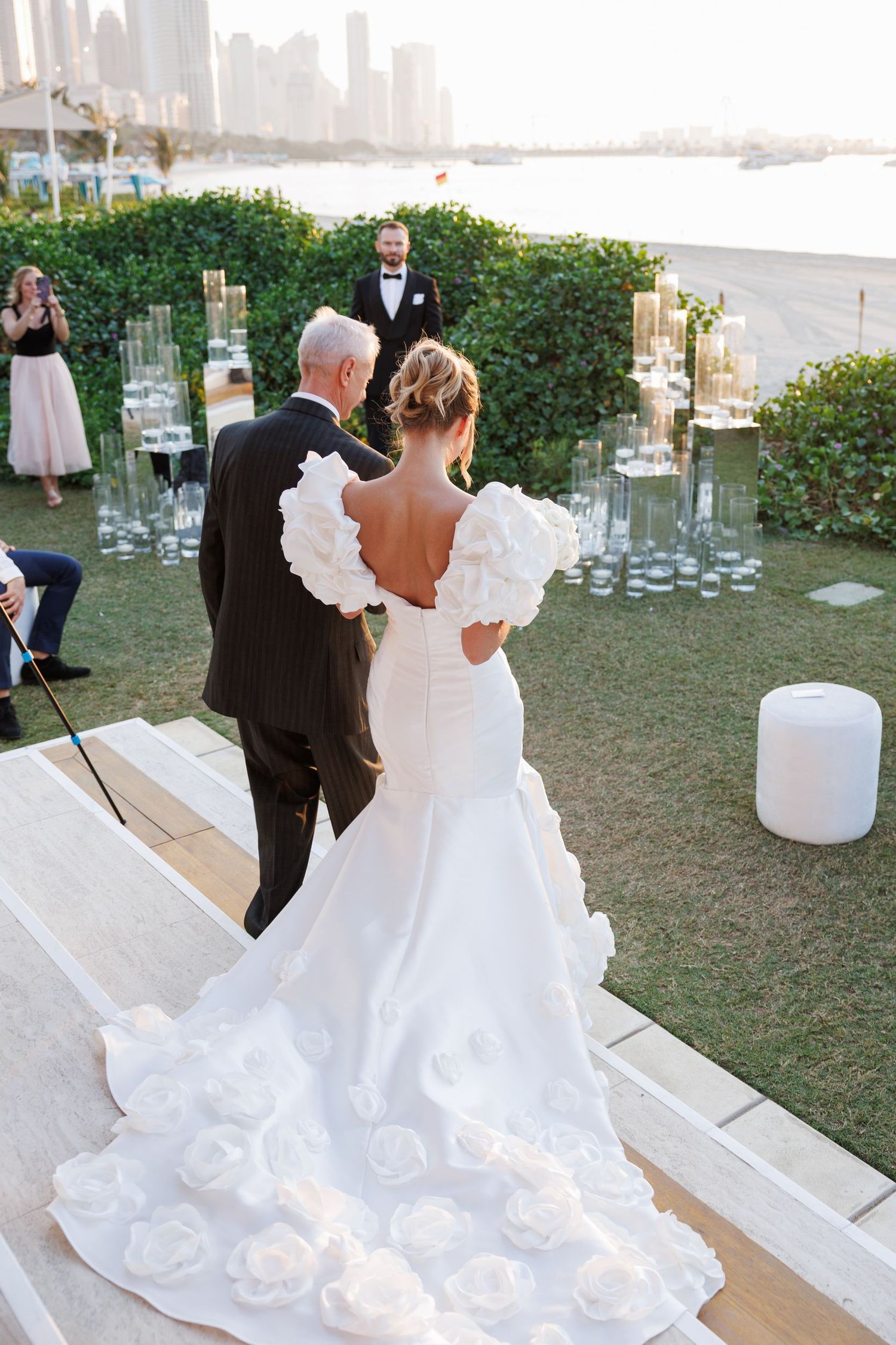 A couple dancing at an outdoor wedding reception with a cityscape backdrop at sunset.