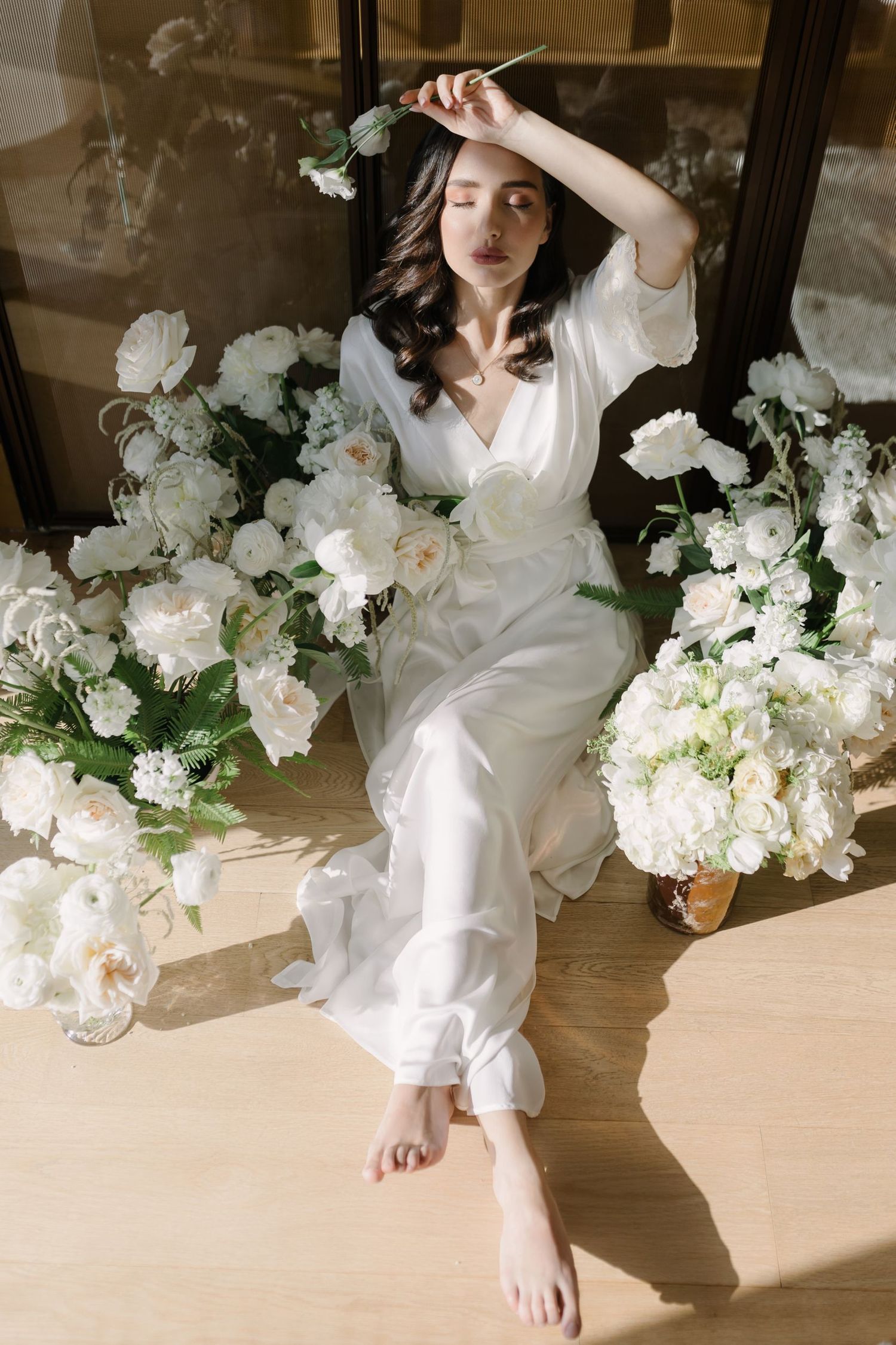 Artistic composition with white flowers and figure in flowing white clothing on wooden floor.
