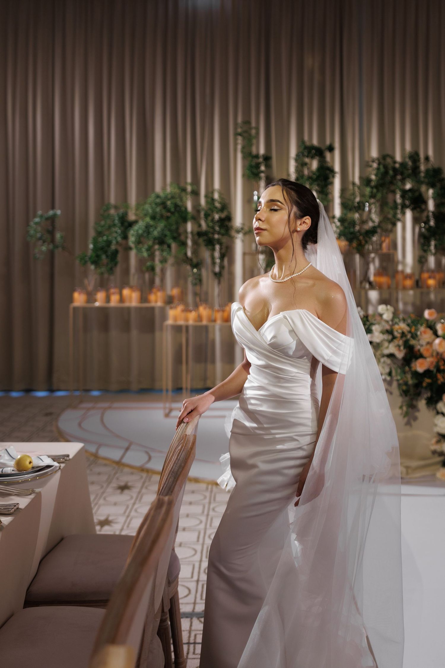 Bride in a sleek white satin gown poses gracefully in an elegantly decorated venue.