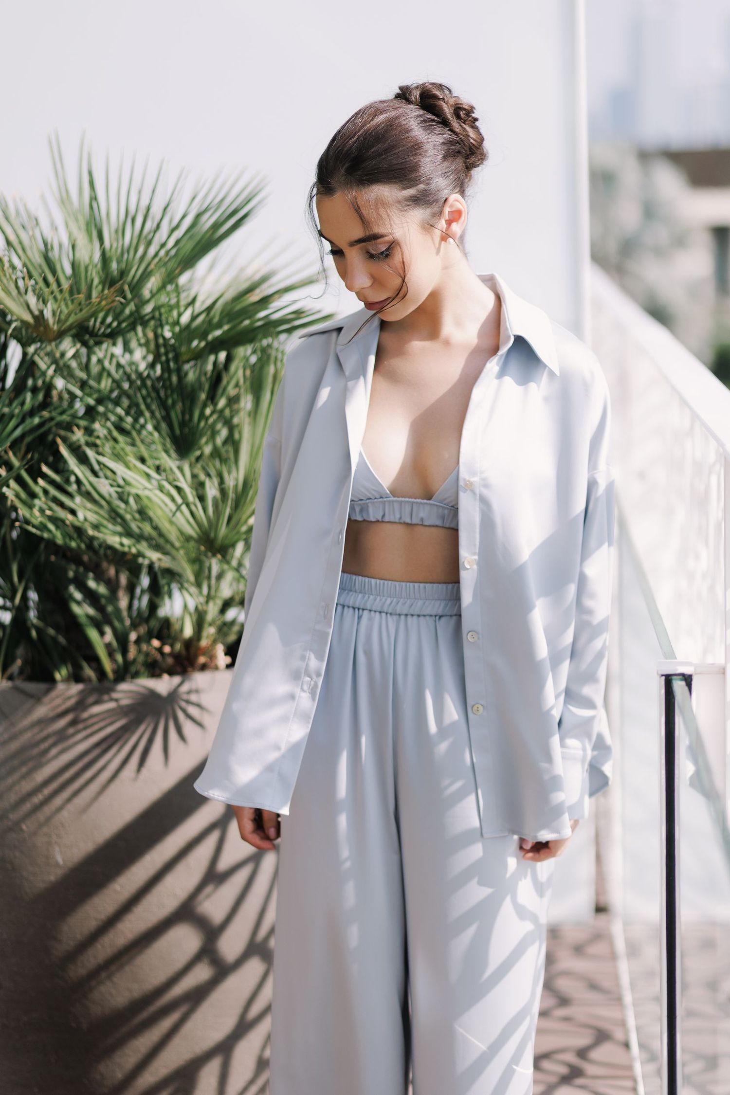 Casual fashion portrait featuring light blue coordinated loungewear set with palm plants.
