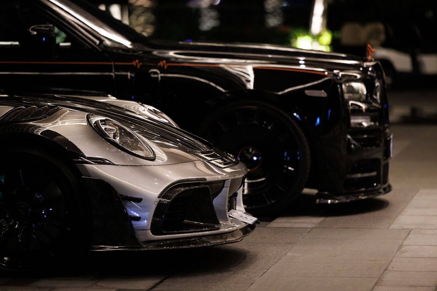 Dark silhouettes of luxury sports cars lined up in a dimly lit showroom.