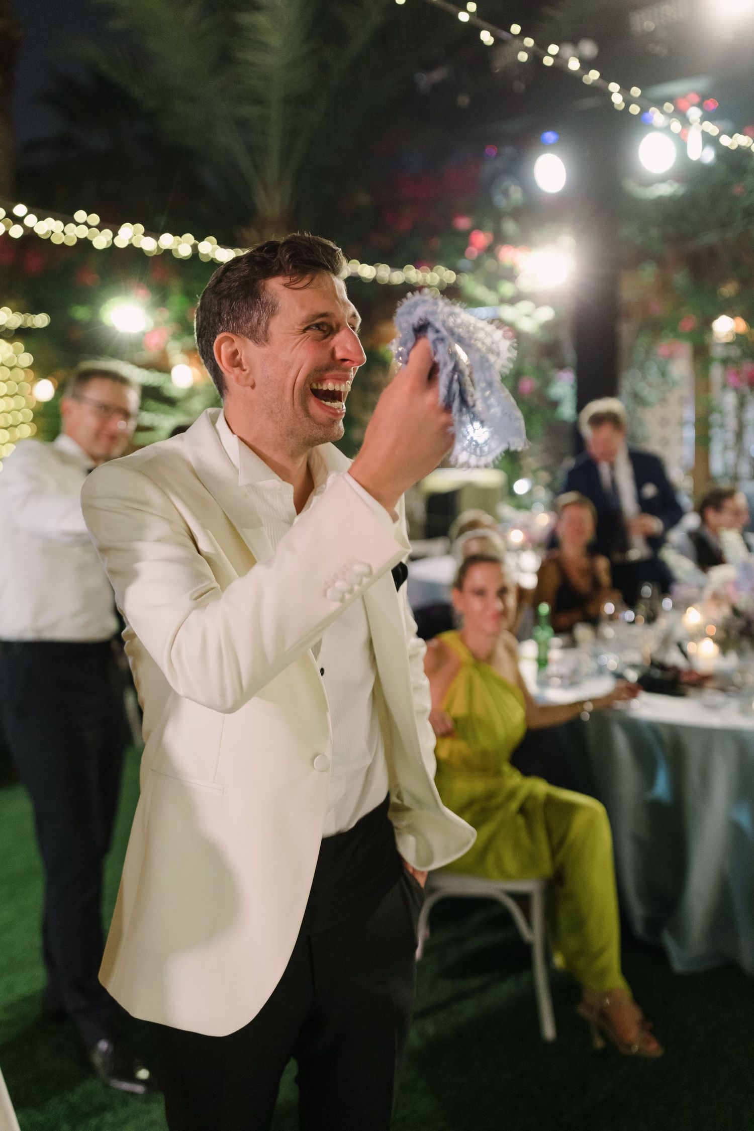 Guest in white jacket dances enthusiastically at outdoor evening wedding reception.