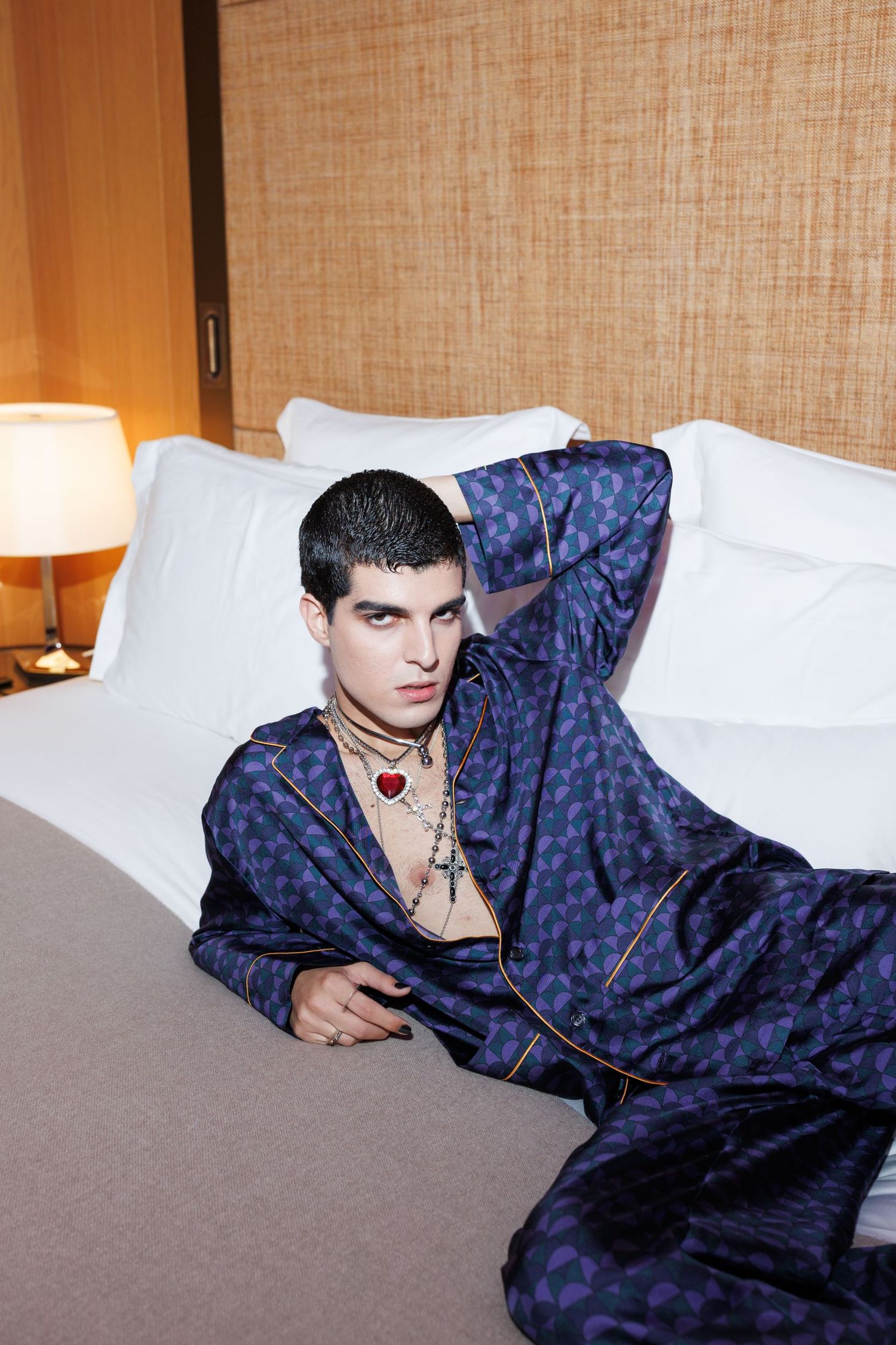 Model in navy patterned outfit poses dramatically on white bedding.