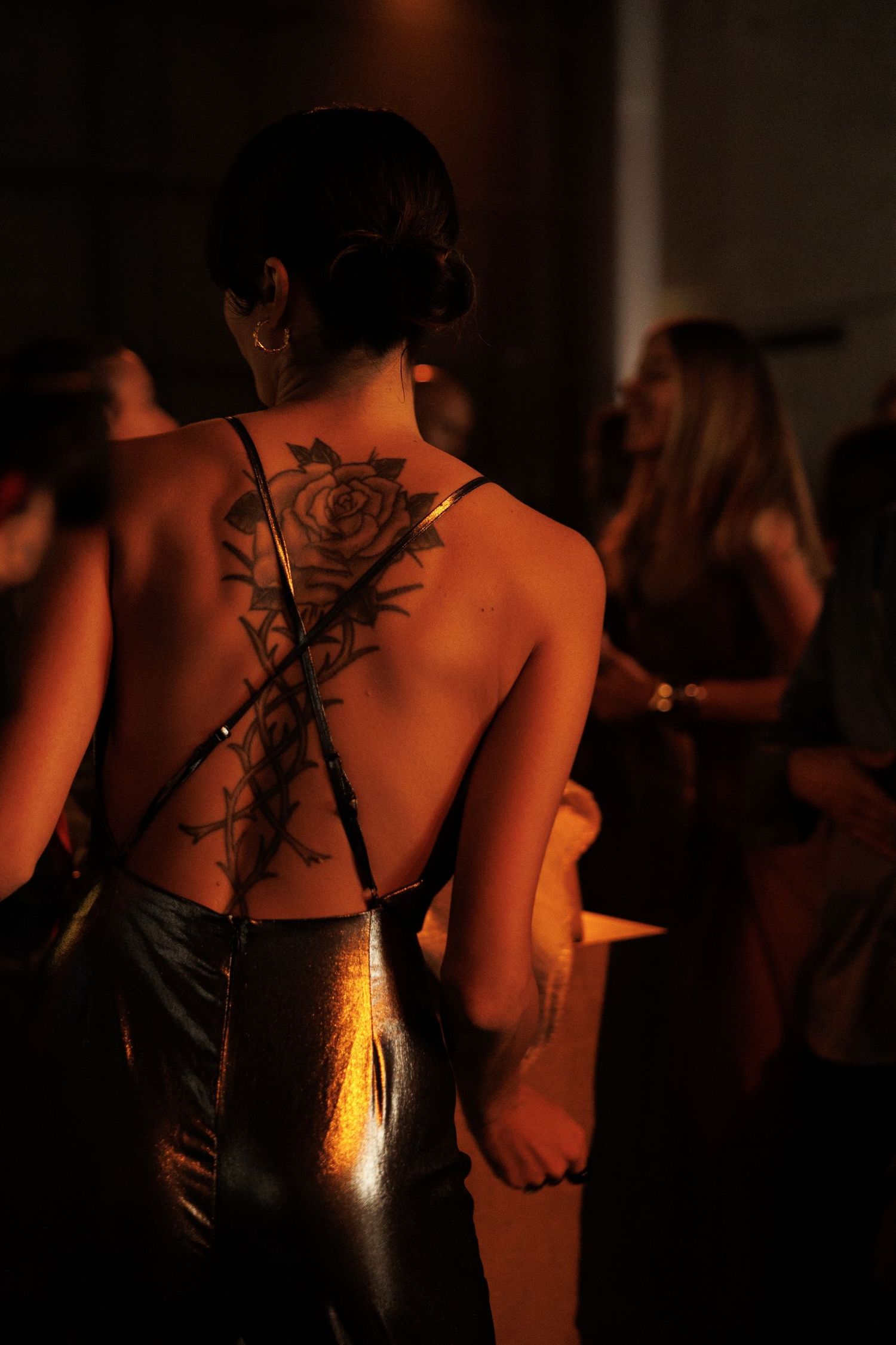Silhouetted figures in dark clothing illuminated by warm spotlights at a nighttime event.