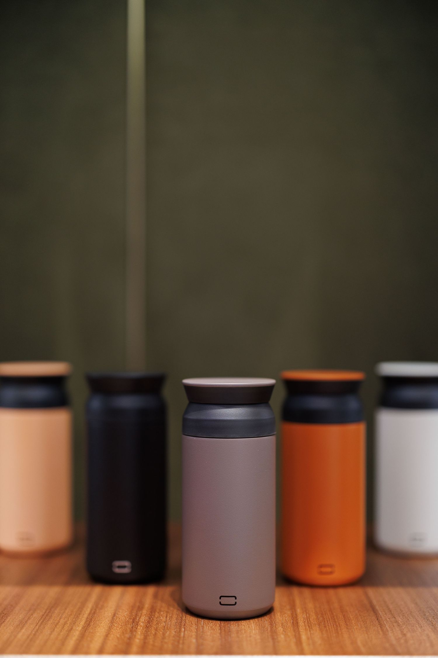 A row of minimalist cylindrical containers in various colors including orange, gray, and white sit on a wooden surface.