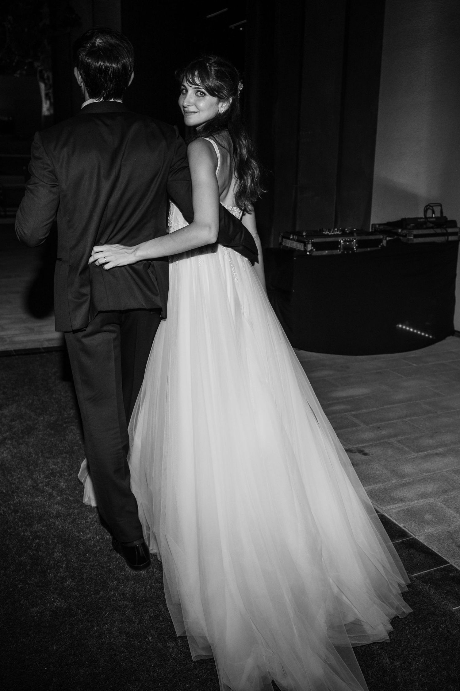 A couple in wedding attire dances together on a wooden floor during their reception.