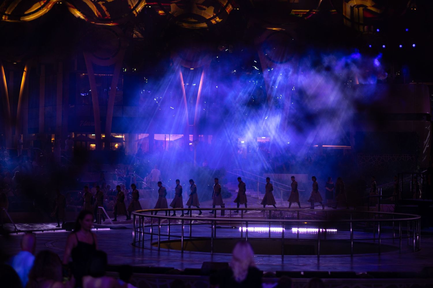 Theater stage bathed in atmospheric blue lighting with silhouettes of performers visible.