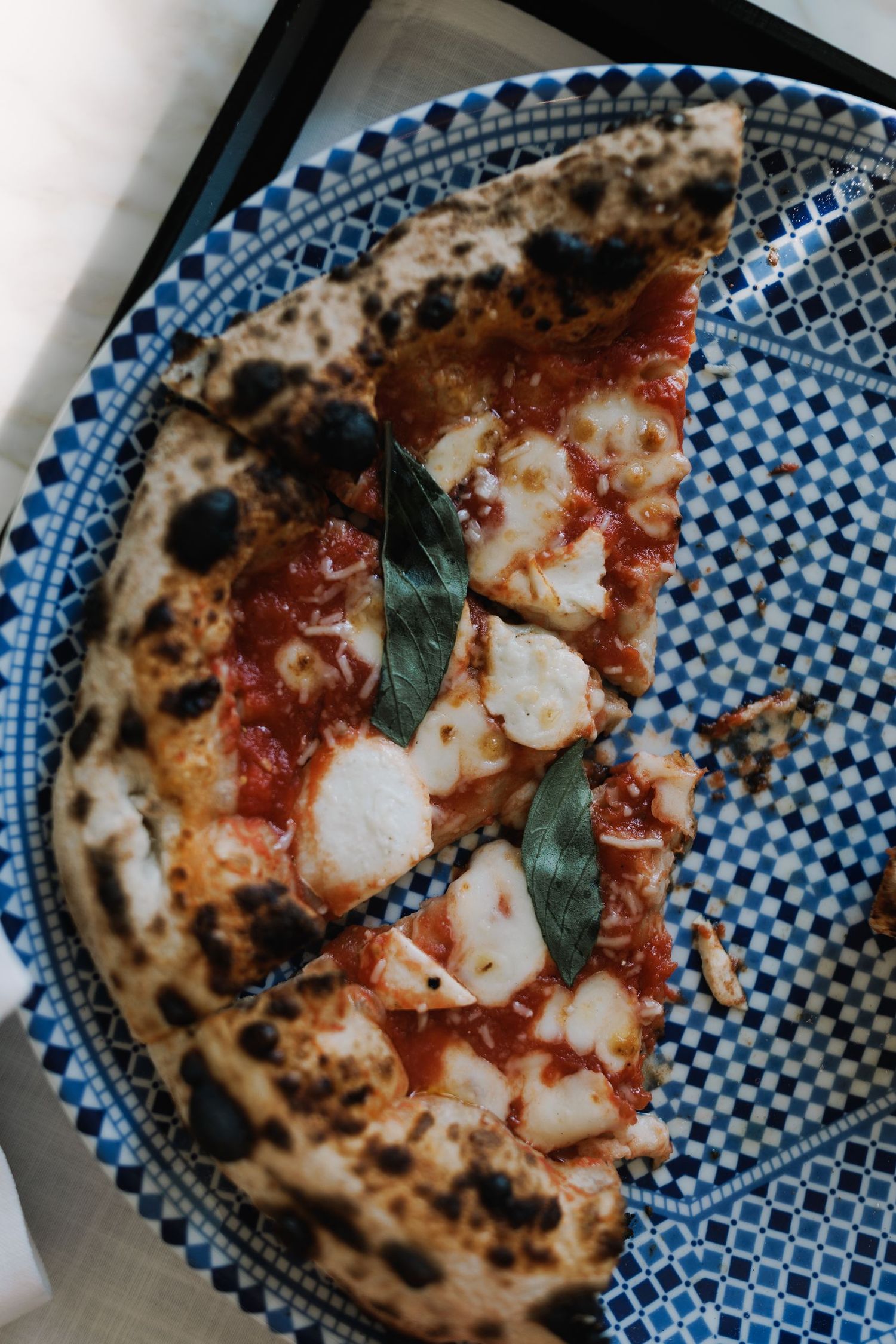 Neapolitan pizza with fresh mozzarella and basil on a decorative blue and white plate.