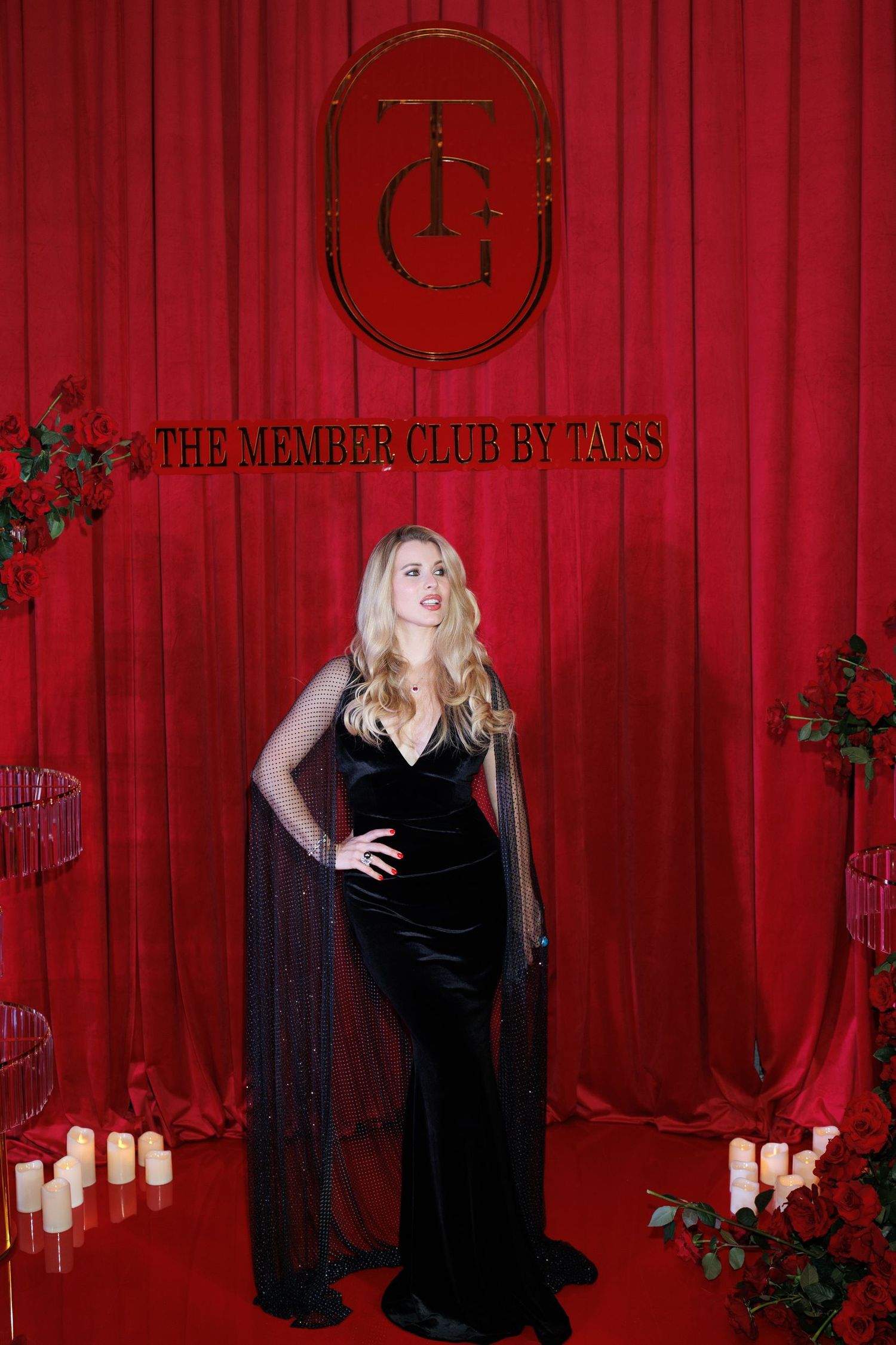 Dramatic black velvet gown with cape photographed against red curtain backdrop.