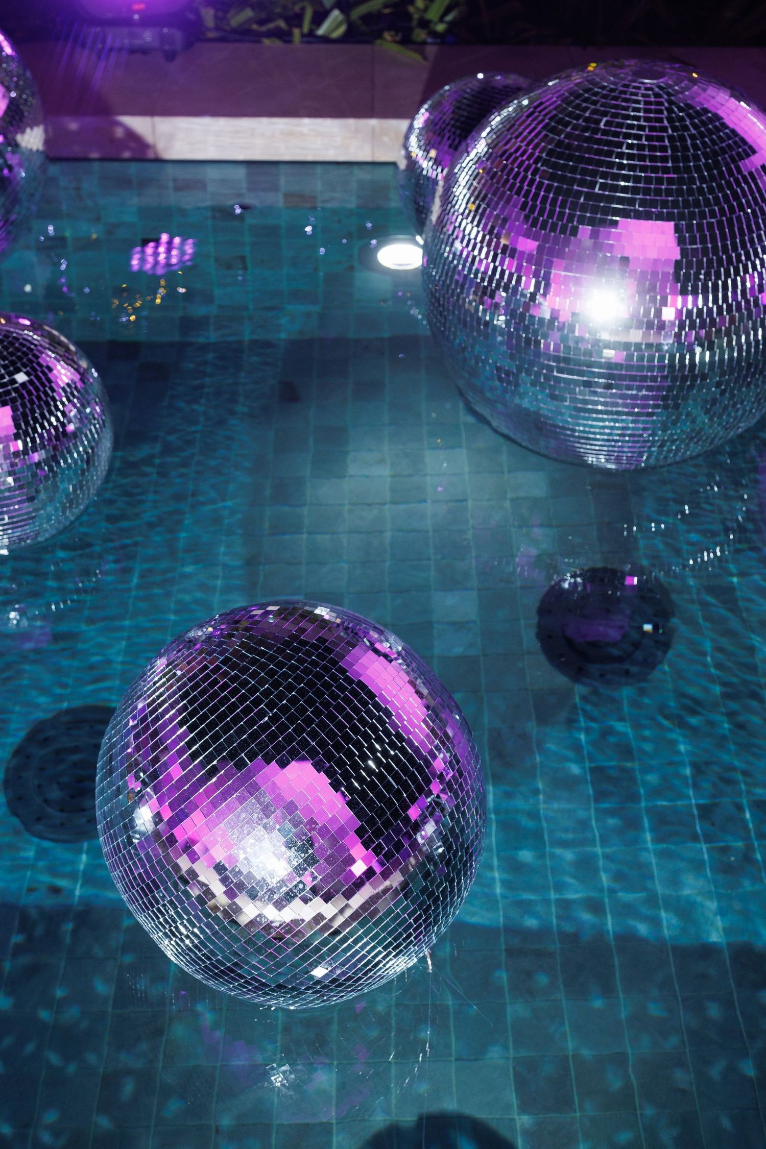 Disco balls reflecting colorful lights over a swimming pool create a party atmosphere.
