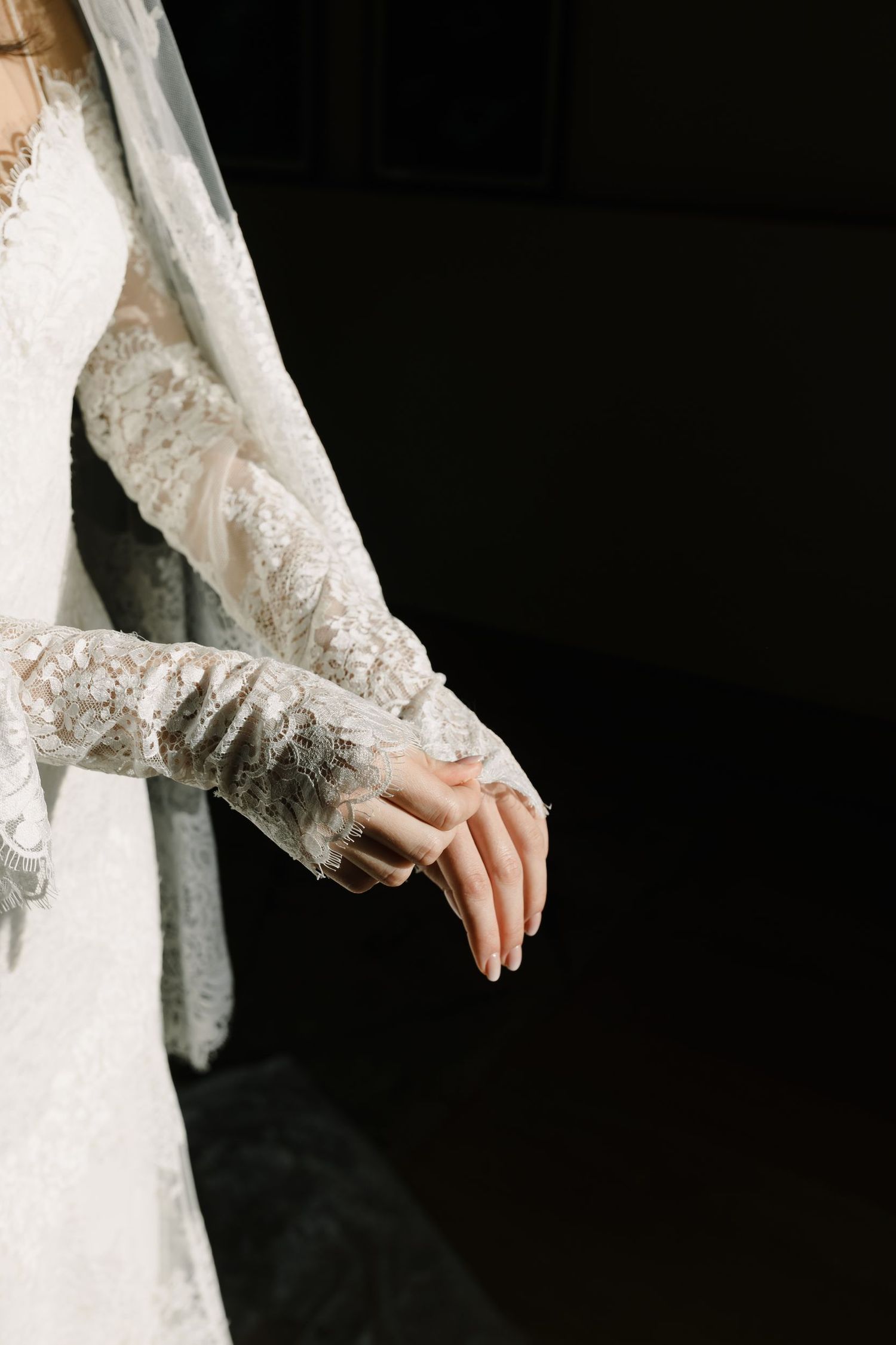 Close-up detail of lace sleeves and hands on a white wedding dress.