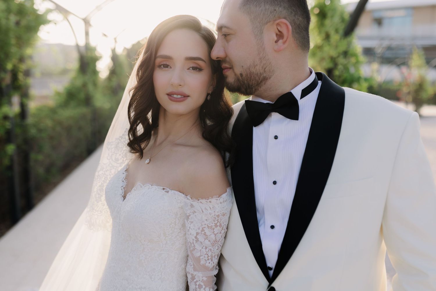 A romantic wedding couple poses together outdoors in formal attire.