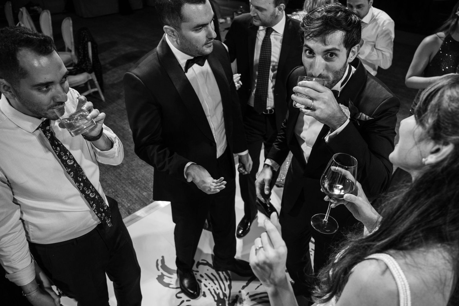 A group of formally dressed guests share drinks and conversation at a wedding reception.
