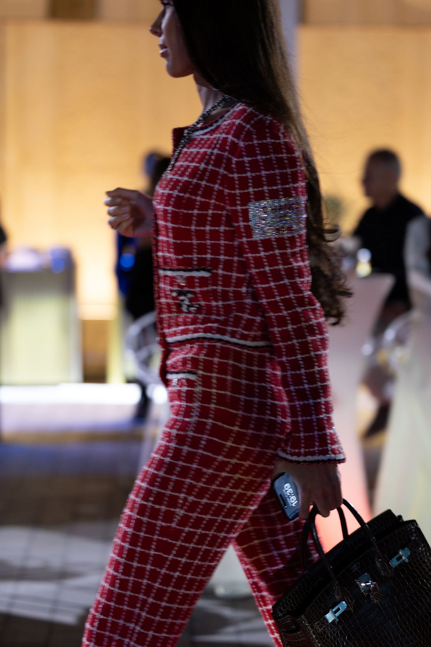 Person wearing red plaid outfit carrying a designer handbag in an upscale setting.