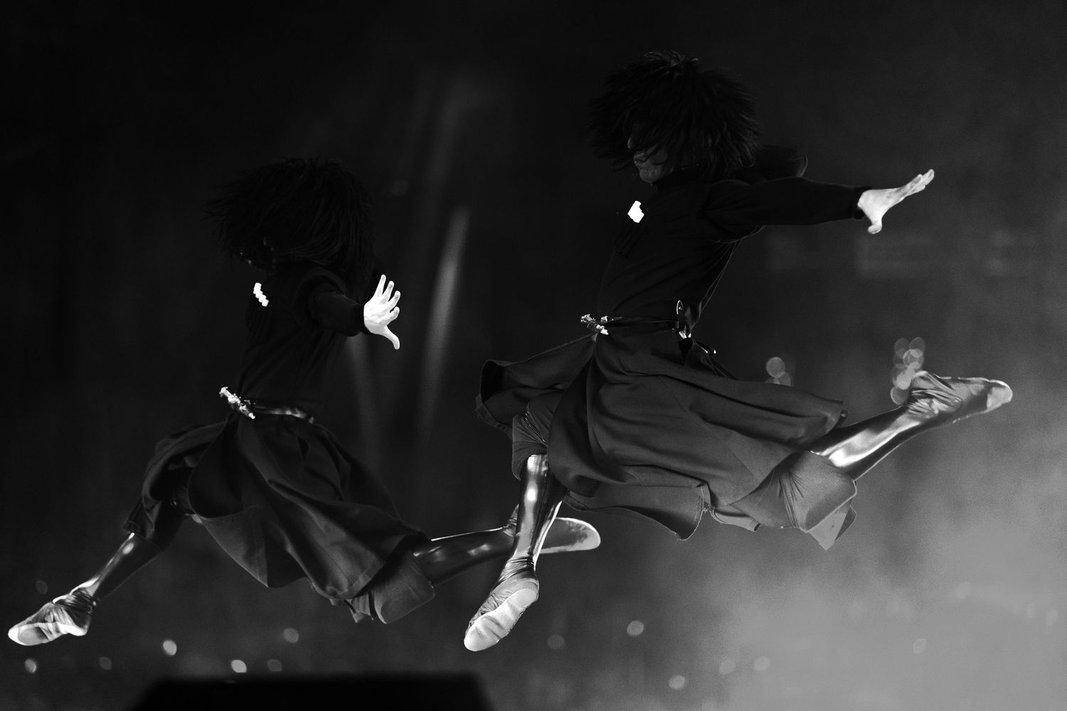 Artistic black and white photograph showing multiple figures in motion across a stage.