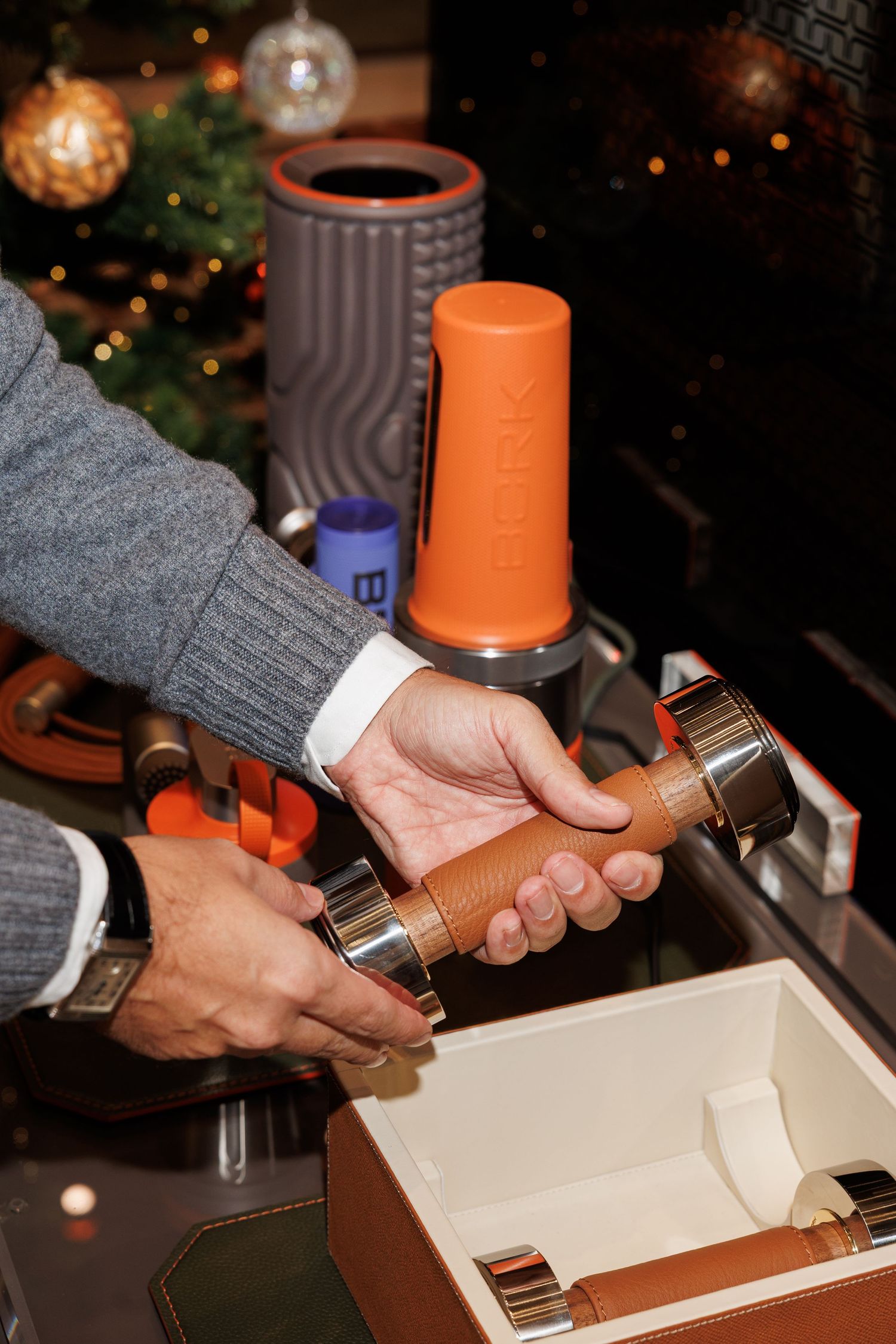 A sequence of hands assembling a wooden box with leather straps and metal hardware in a Christmas setting.