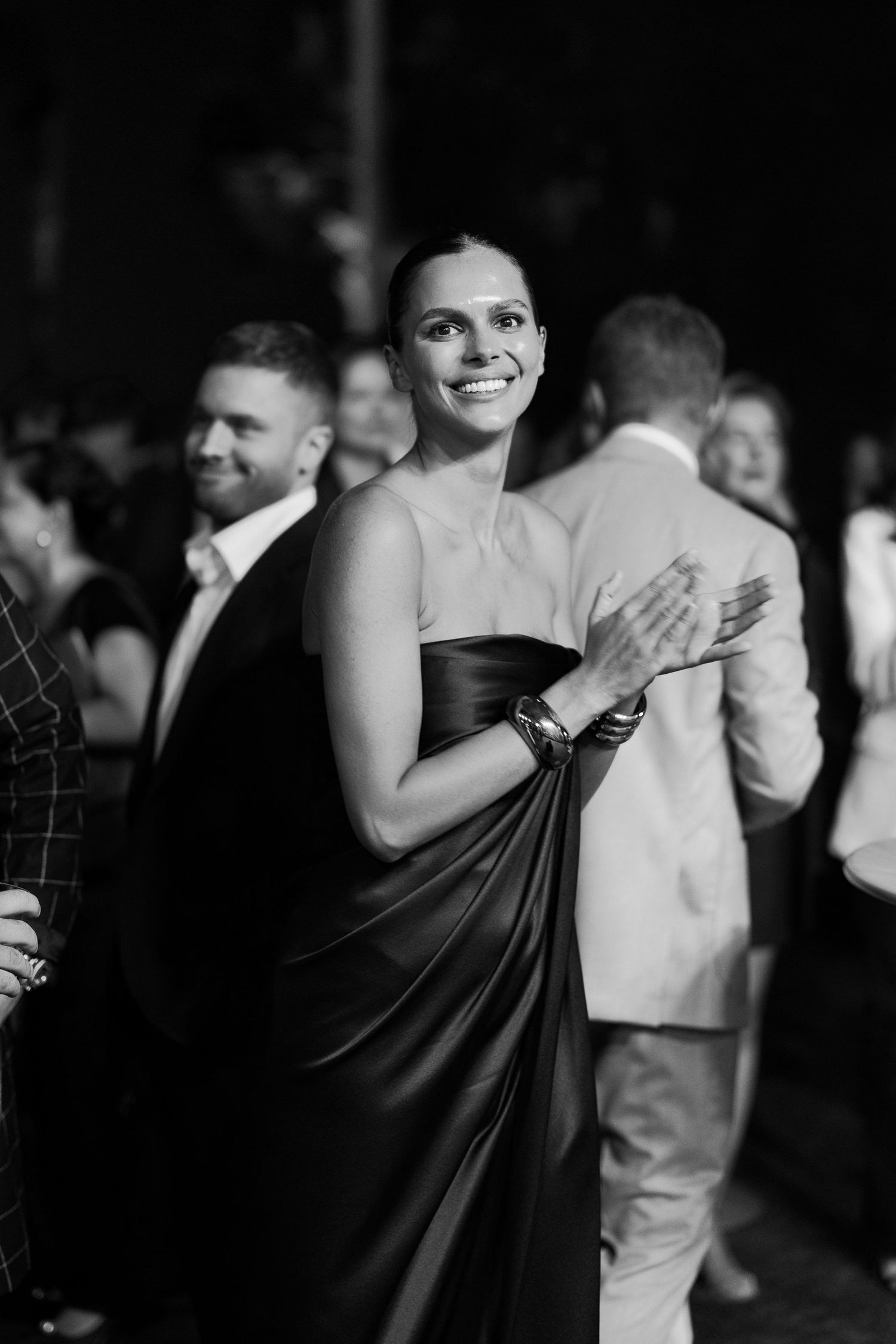 A person in an elegant black strapless gown smiles while attending a formal event in black and white photography.