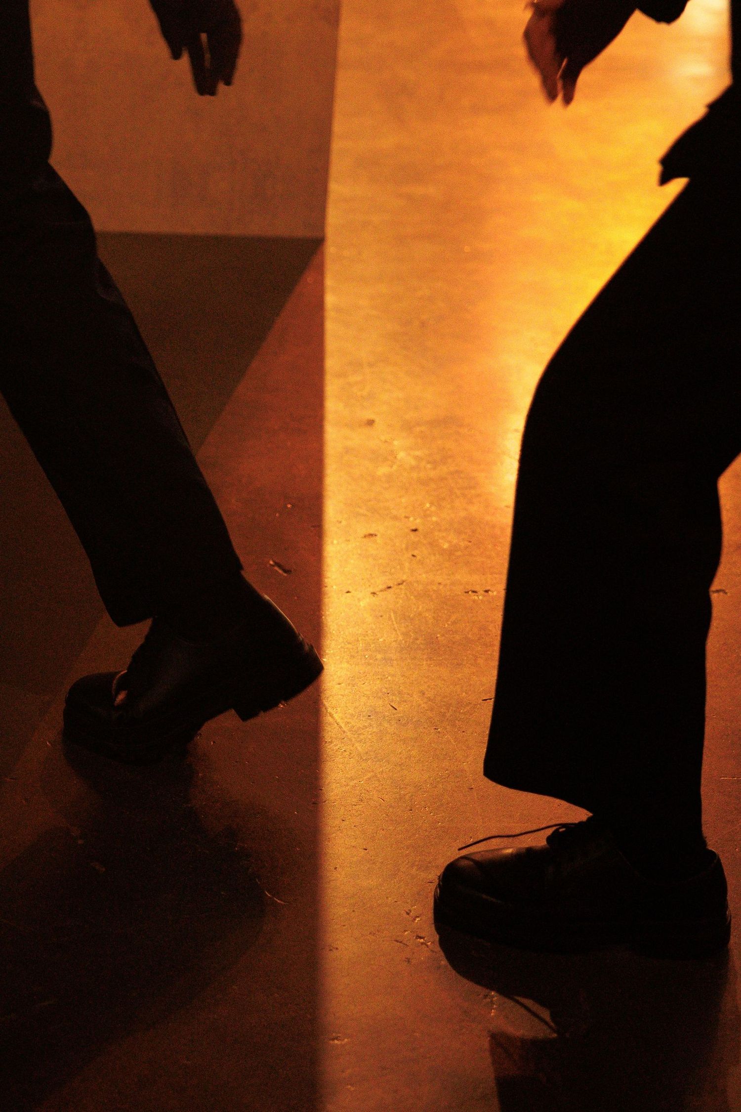 Silhouettes of people walking across warmly lit floor in art gallery space.