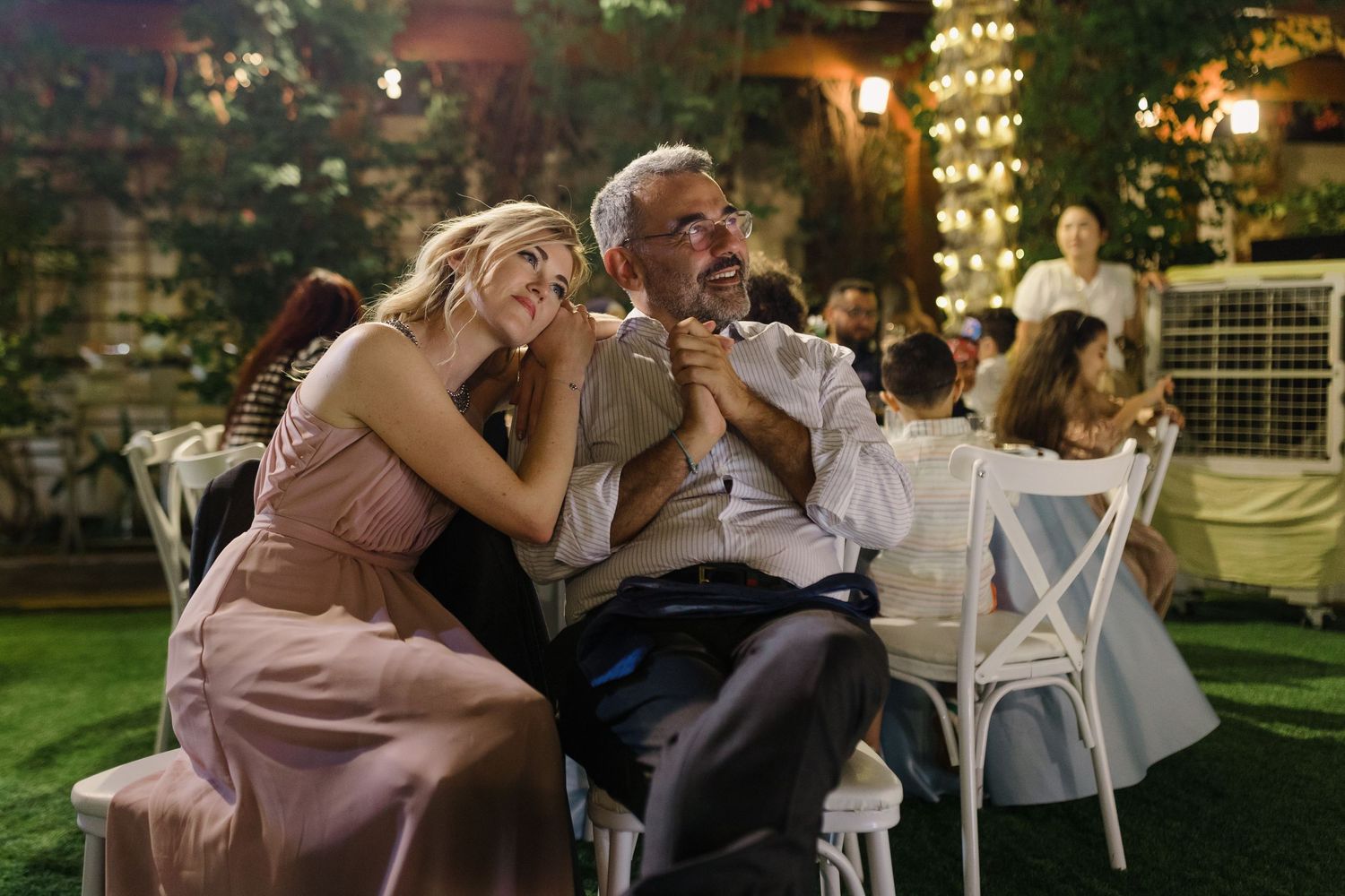 Wedding guests dance and celebrate during evening outdoor reception under string lights.