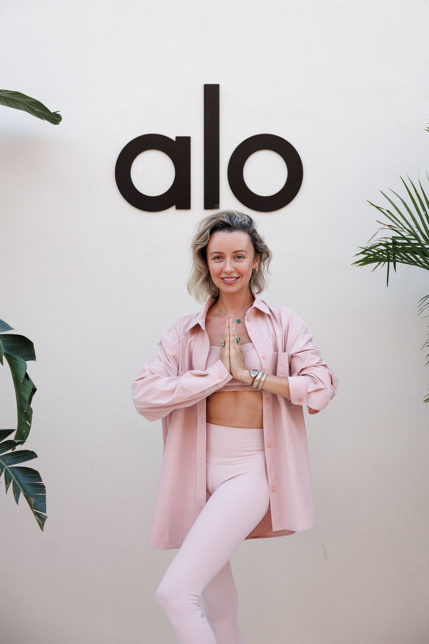 Pink activewear displayed against white wall with Alo branding.