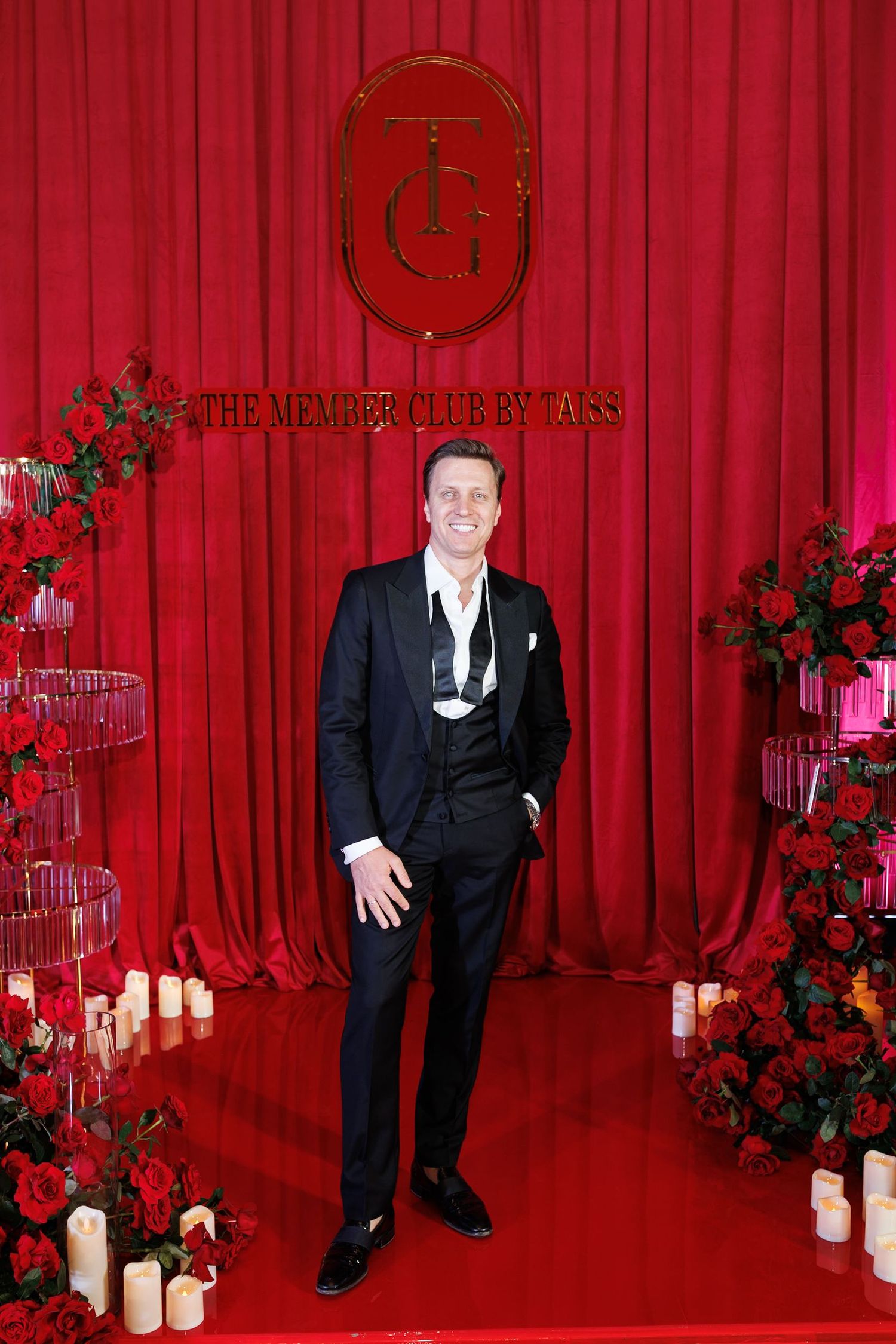 Elegant event setup with red curtain backdrop, logo signage, and floral arrangements at The Member Club by Taks.