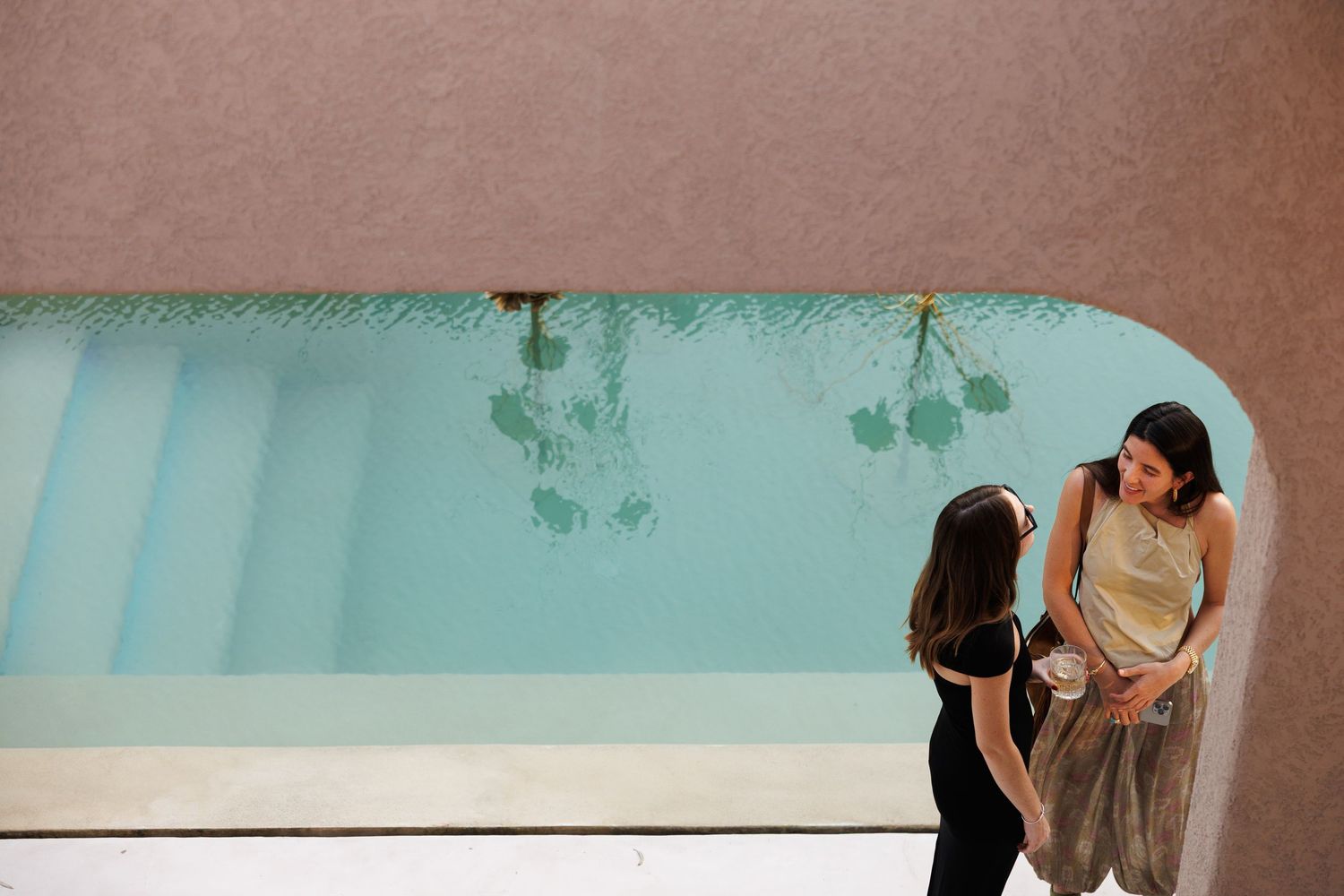People in conversation near turquoise pool in minimalist indoor space.