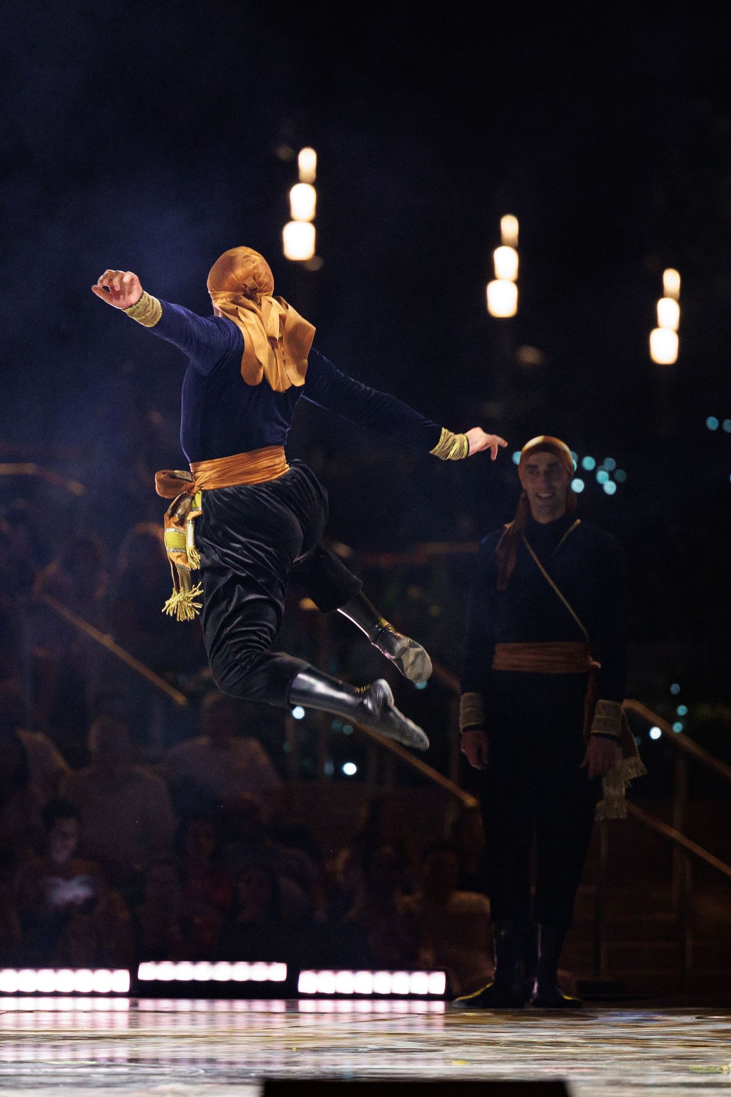 Performer in navy costume executing a dramatic aerial jump on stage.