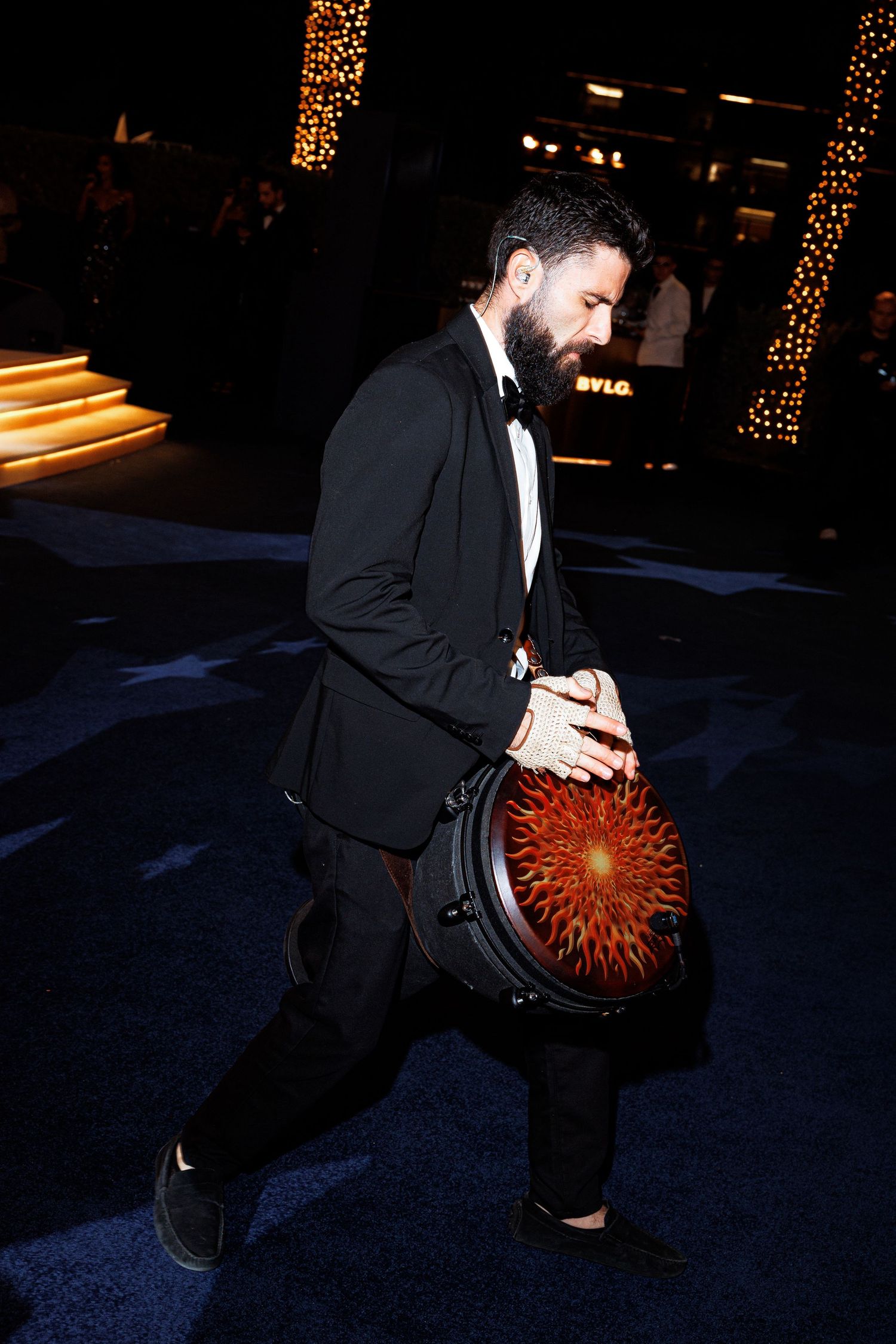 A person in a black suit kneels on a dark floor while holding a glowing red sphere.