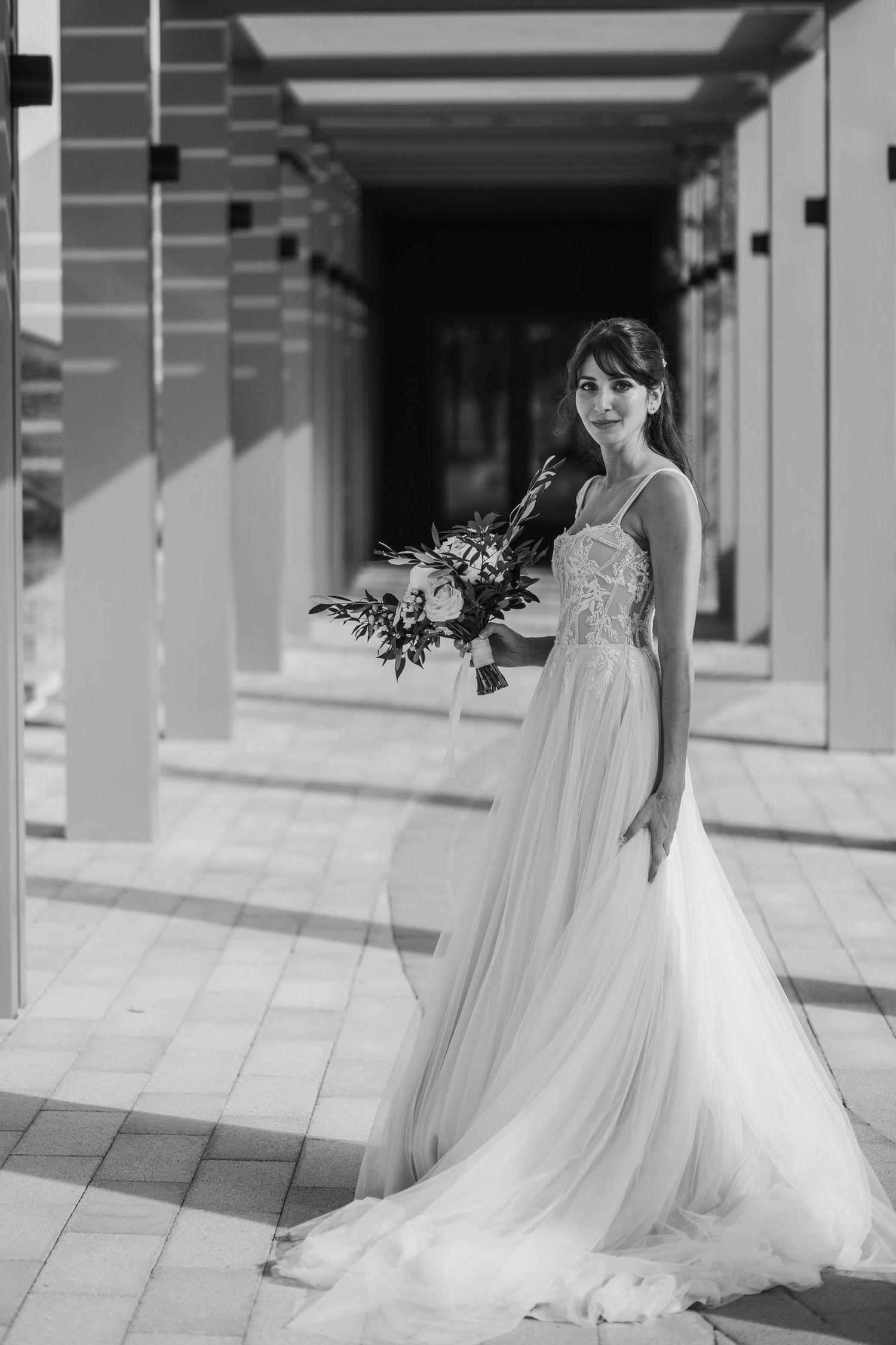 Elegant white wedding dress with flowing train photographed in a bright corridor with columns.