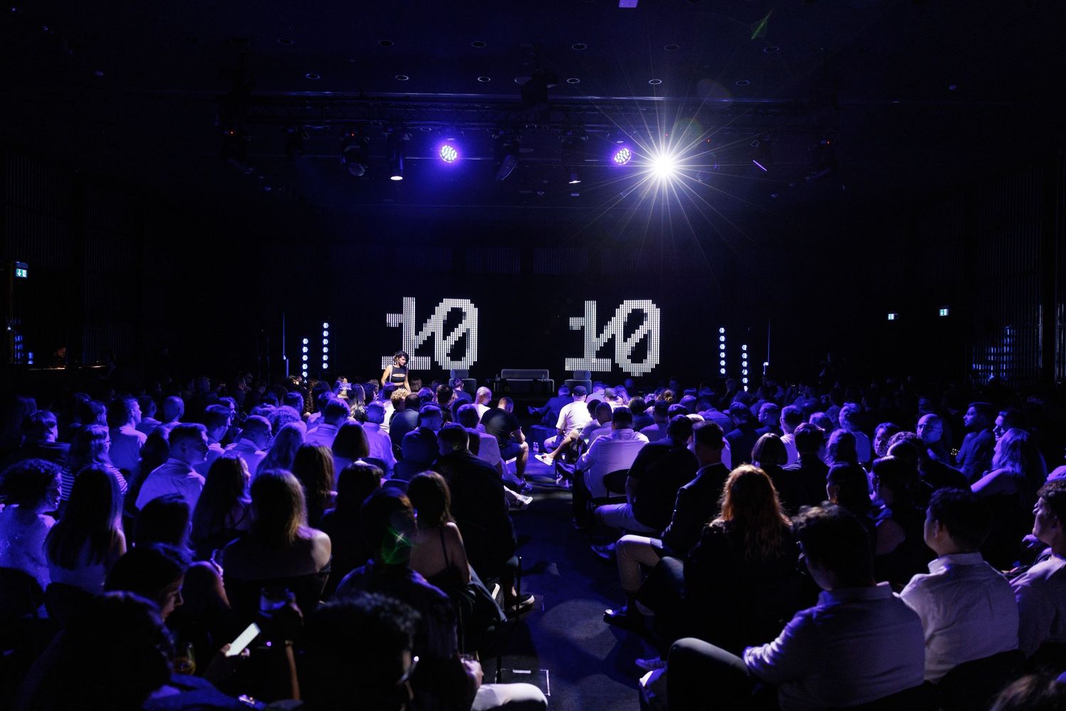 Dark auditorium filled with audience members under blue lighting.
