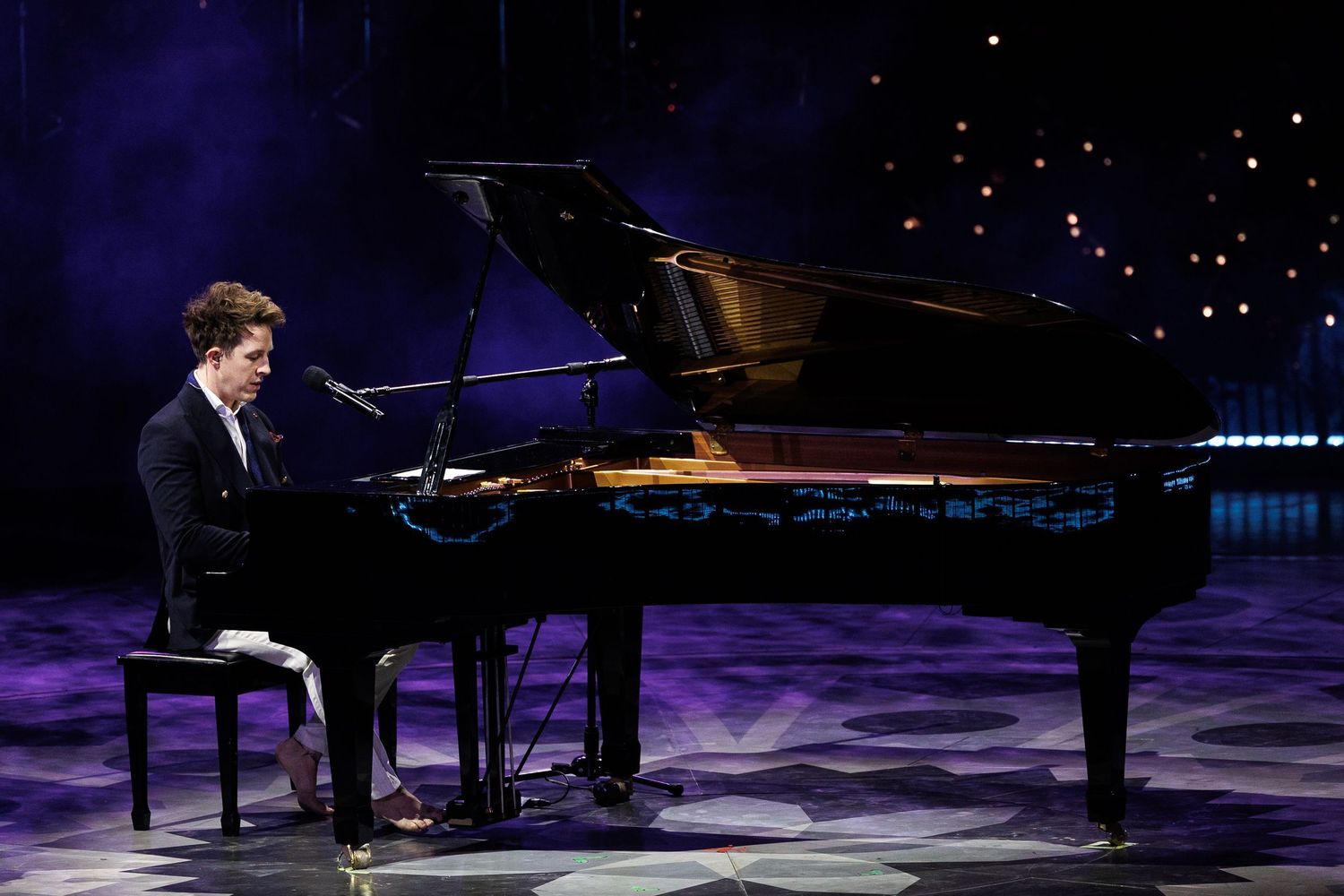 Grand piano sits illuminated on stage during an ice skating performance.