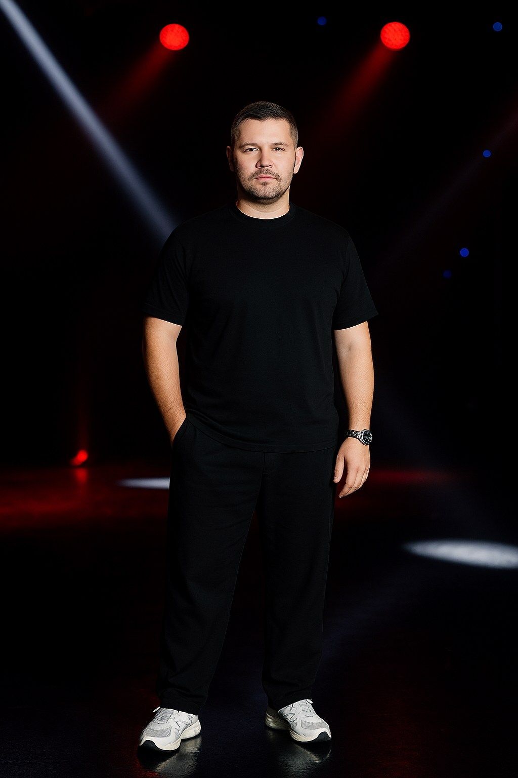 Person in black t-shirt and pants performing on stage with white spotlight.