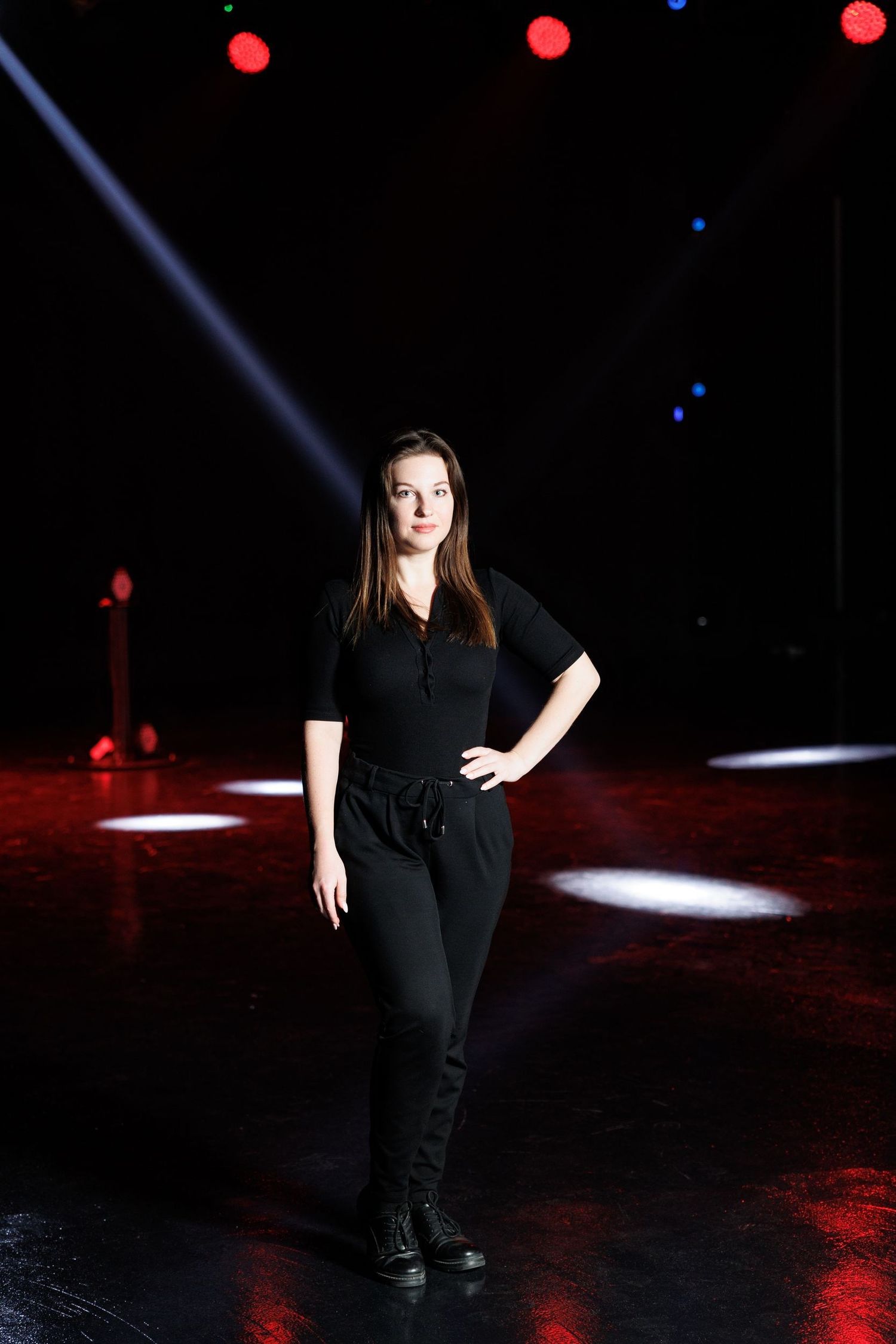 Performer in black attire on dimly lit stage with red and white lighting effects.