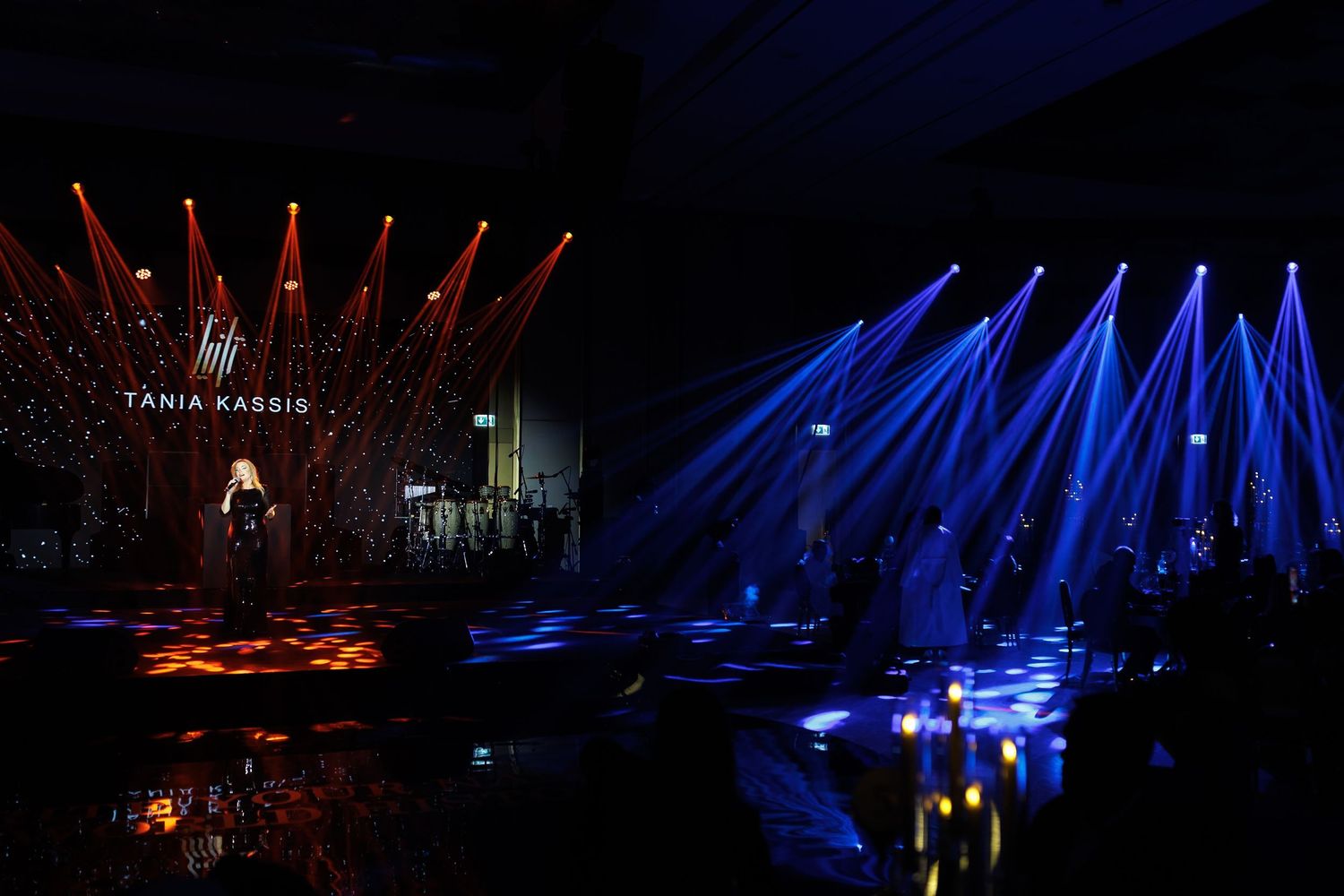 Concert stage illuminated with dramatic red and blue lighting beams creating reflections on stage.