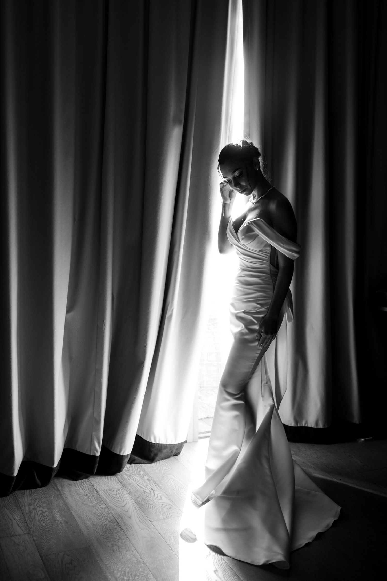 Dramatic silhouette of a bride against window light and curtains.