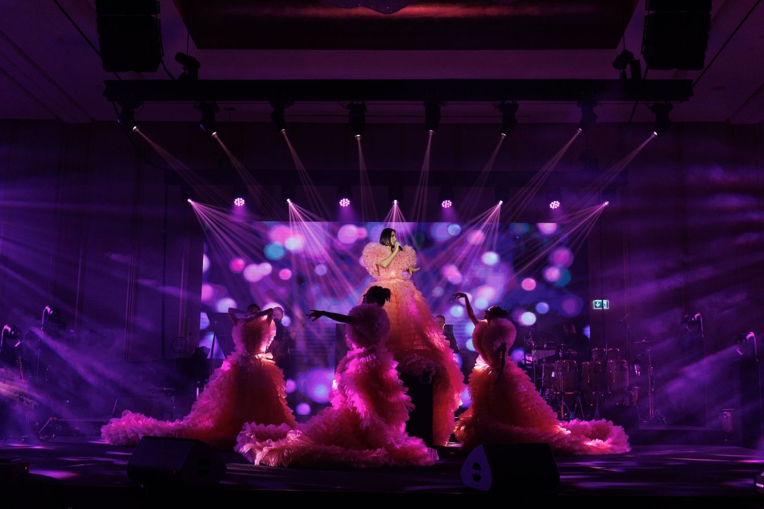 Pink and purple stage lighting illuminates decorative elements against a dark background.