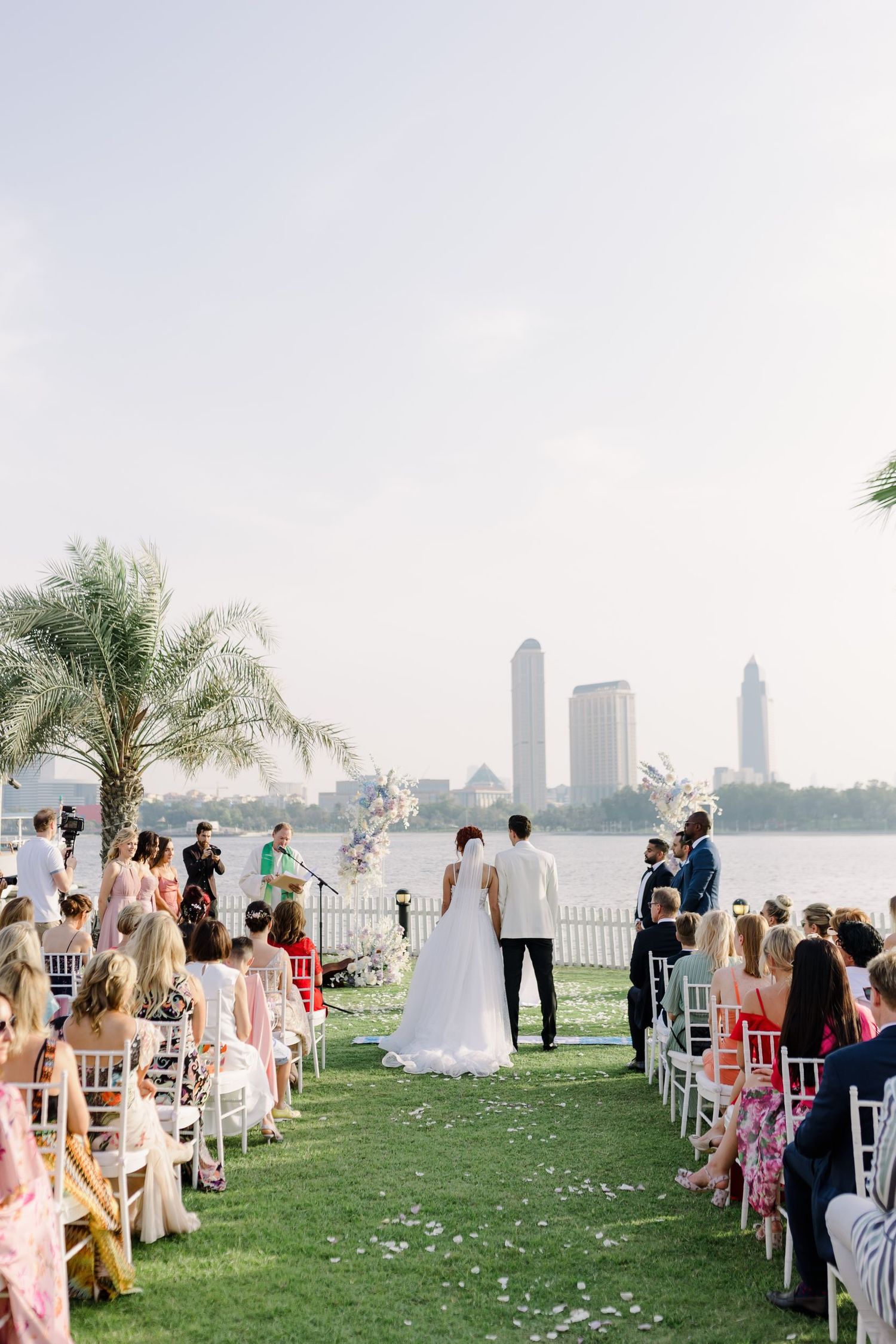 An outdoor wedding ceremony setup with white chairs on grass overlooking a city skyline.