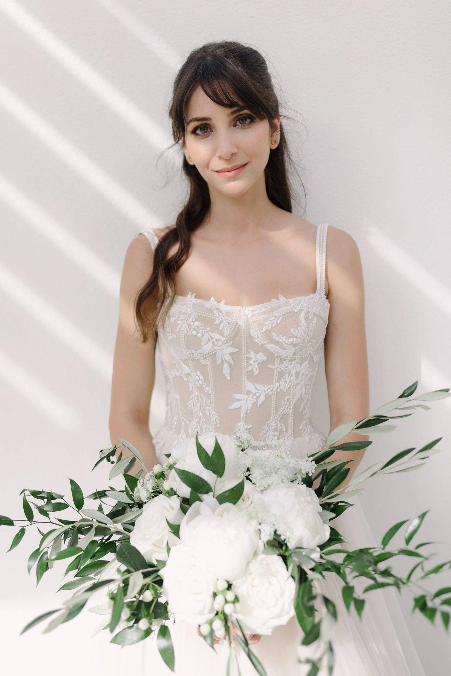 White bridal bouquet with green foliage against a delicate lace wedding dress.
