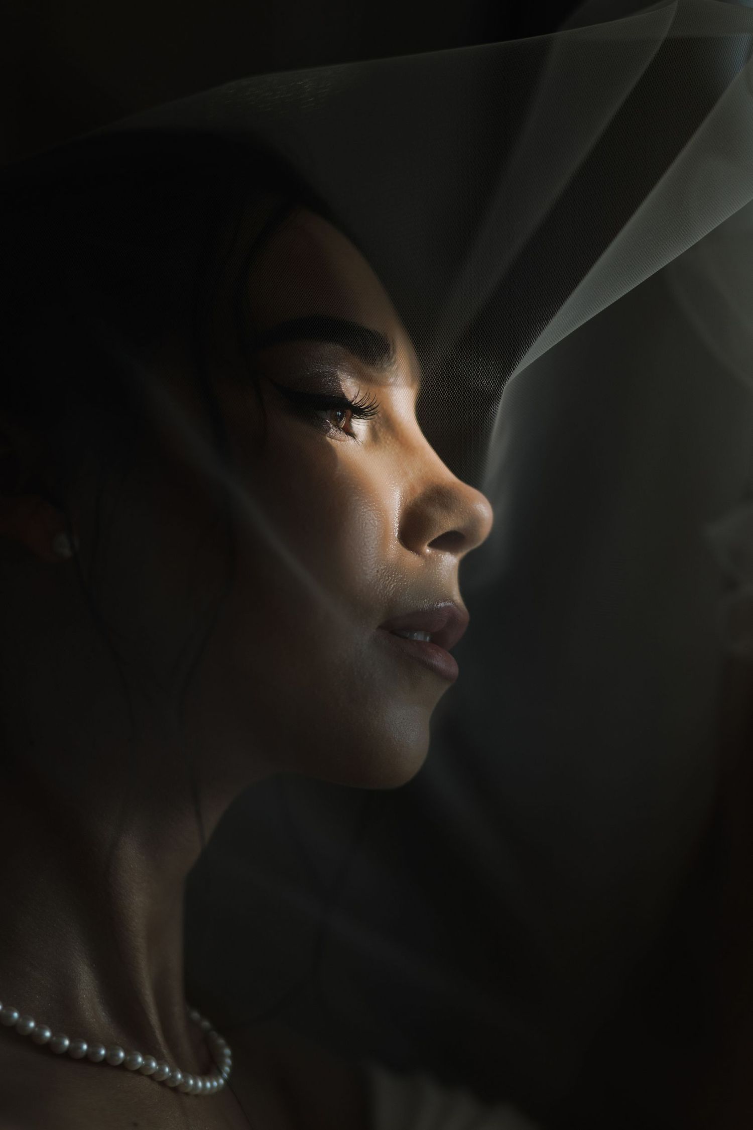 Artistic portrait with dramatic shadows and pearl necklace detail.