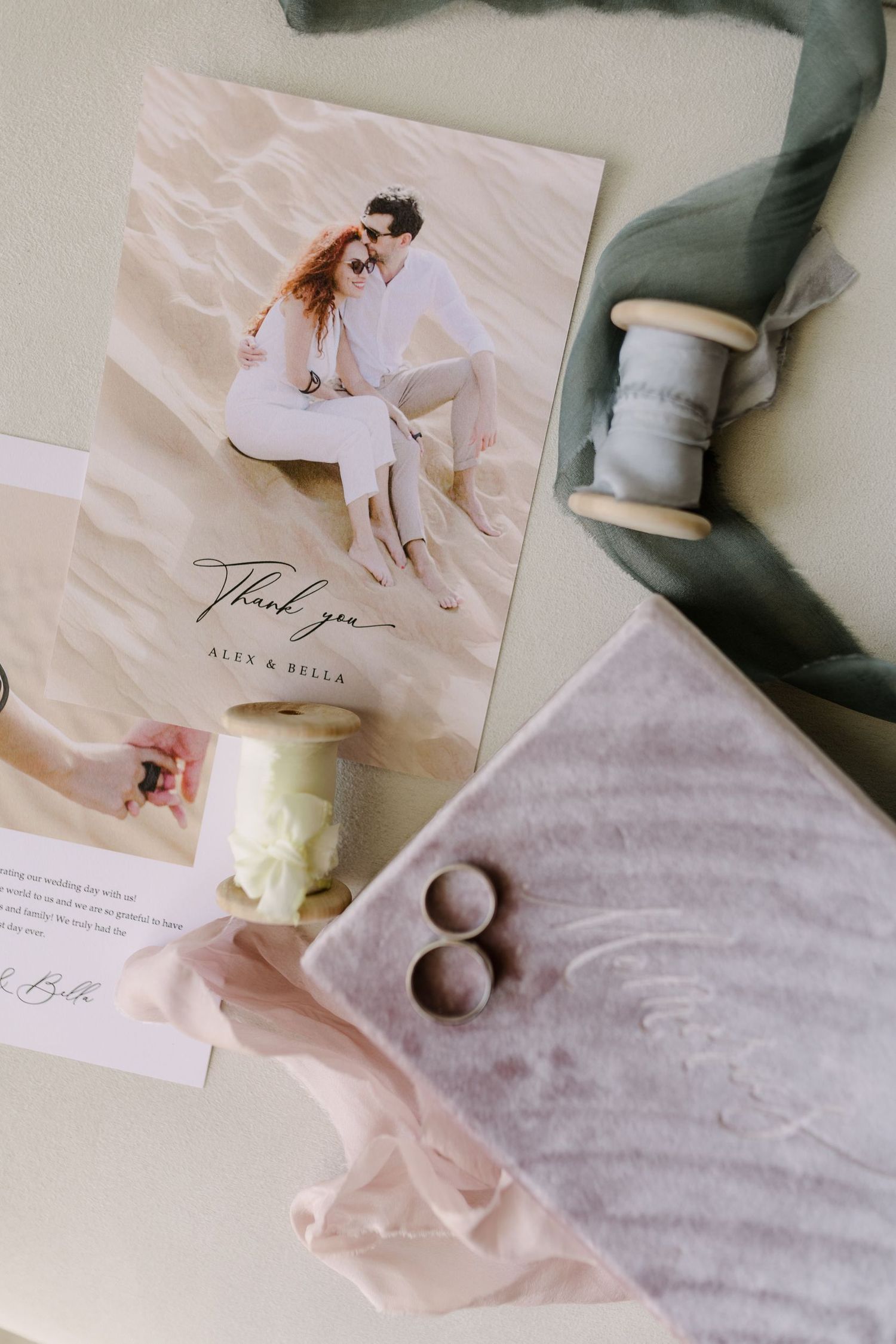 Wedding stationery flatlay with thank you card, silk ribbon, and wedding rings.