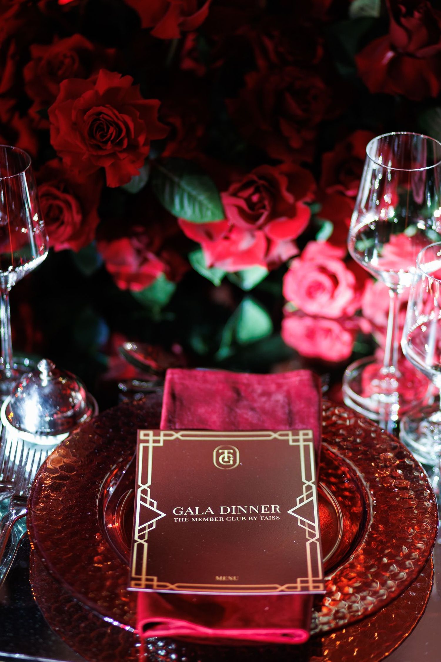 Elegant gala dinner place setting with red roses and crystal glassware.