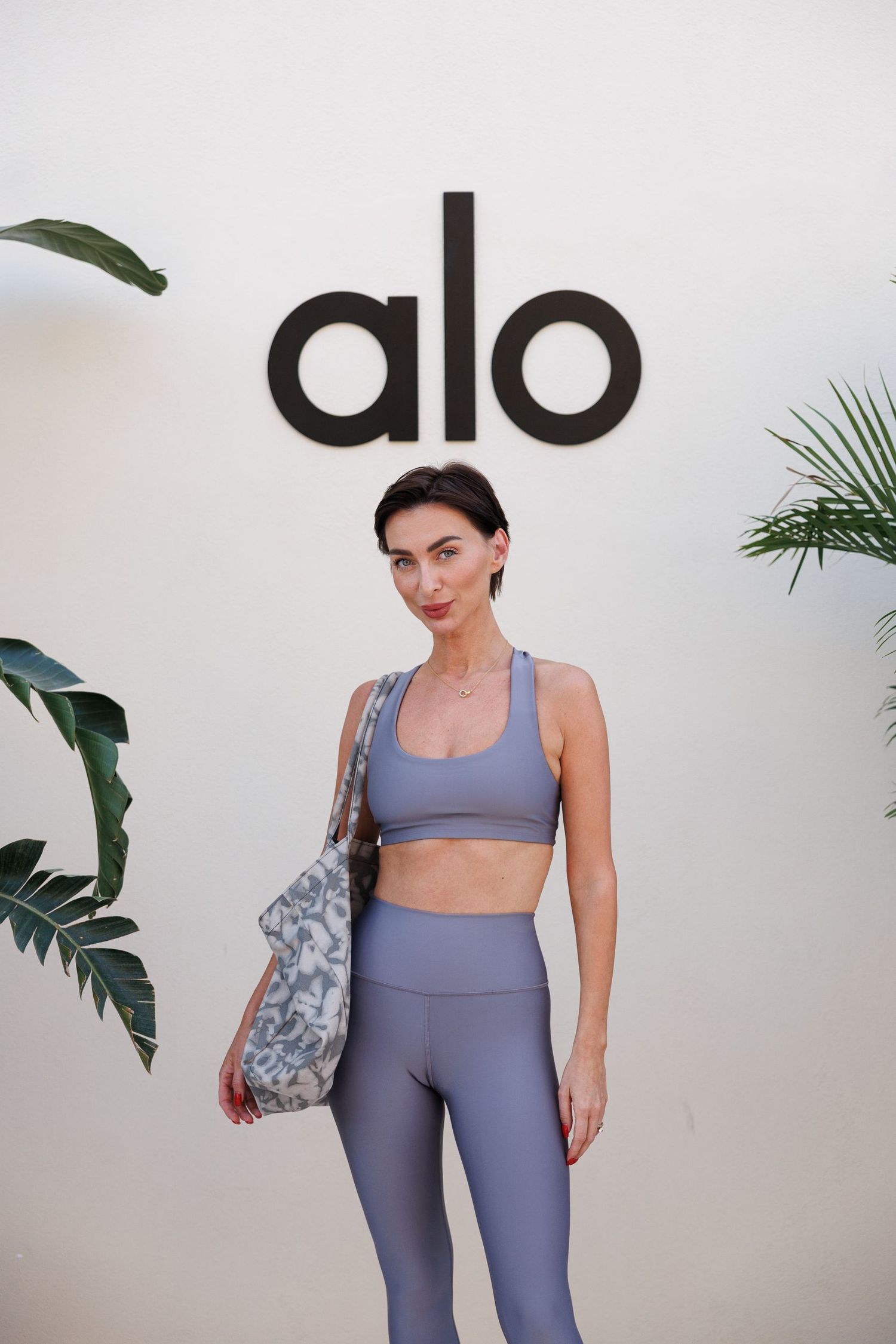 Woman modeling periwinkle blue athletic set against white wall with brand logo.